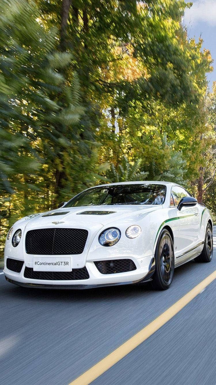 手機 桌布 壁紙 — 一輛白色賓利 Continental GT3R 在綠樹成蔭的道路上高速行駛，動態模糊傳達出高速與奢華感。