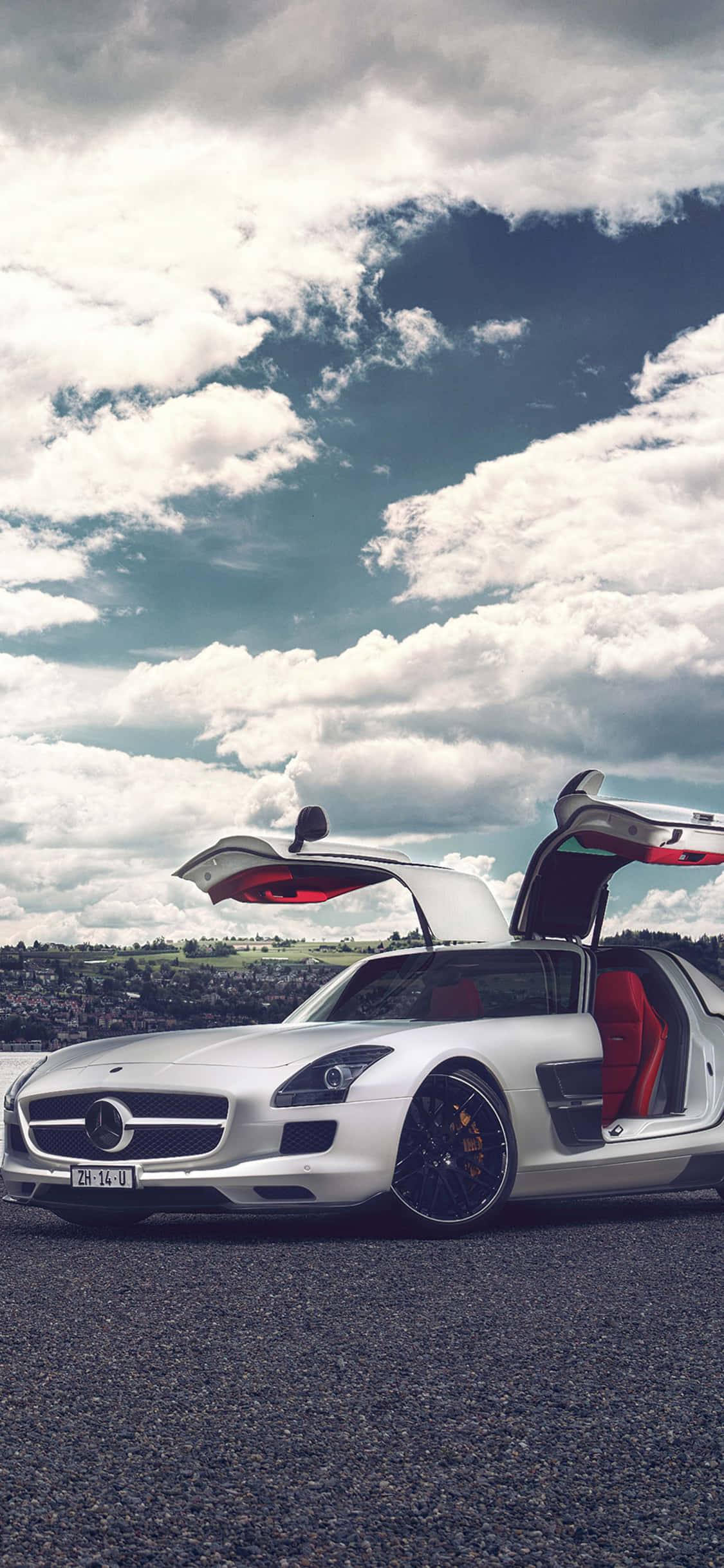 iPhone X Amg Gt-r 桌布 壁紙 — 一輛白色賓士 SLS AMG 跑車，鷗翼車門打開，停在碎石路上，天空烏雲密佈，氣氛戲劇化。