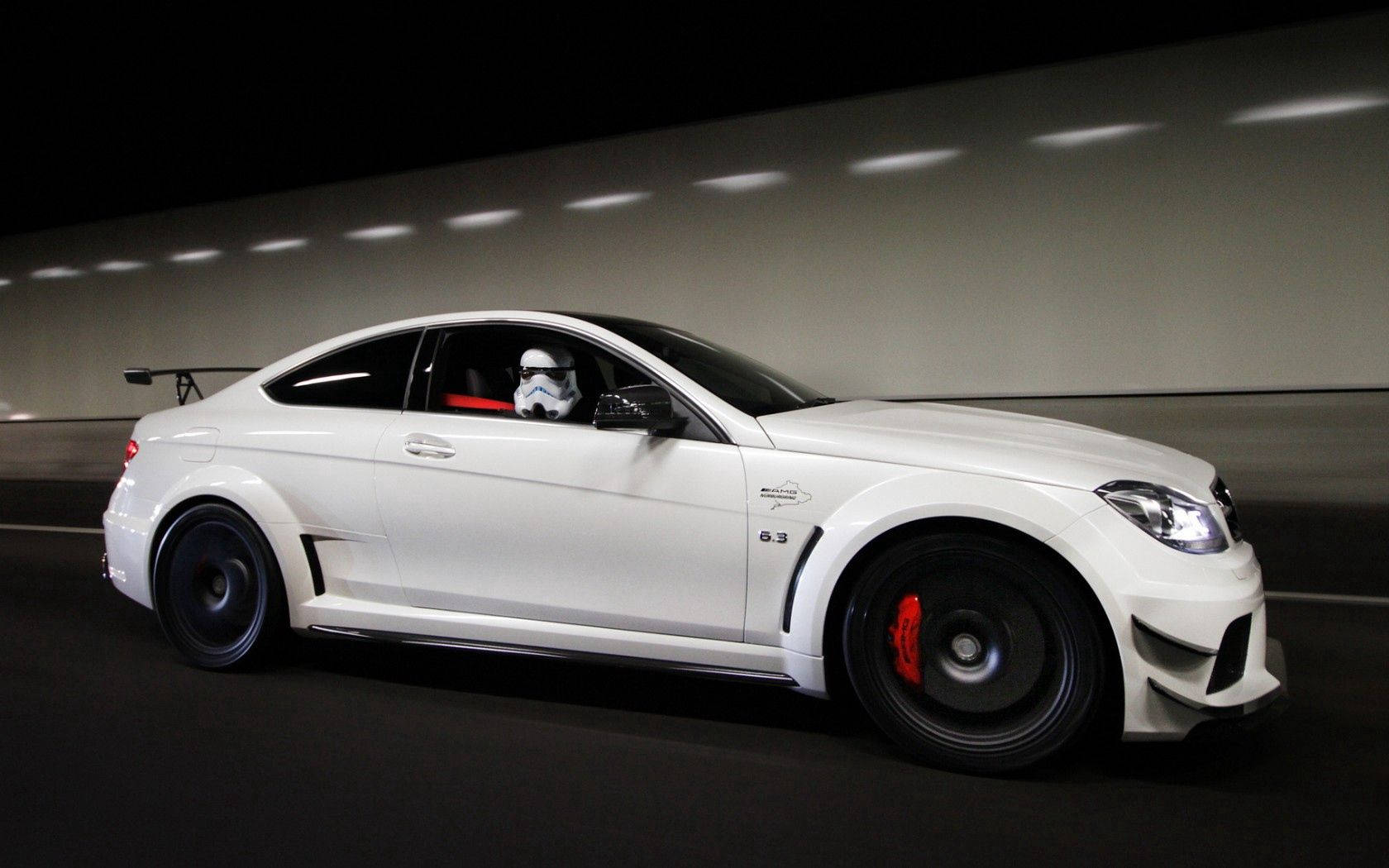 Mercedes 桌布 壁紙 — 一輛白色賓士C63 AMG轎跑車在燈光昏暗的隧道中飛馳，駕駛艙內可見一名風暴兵駕駛員。