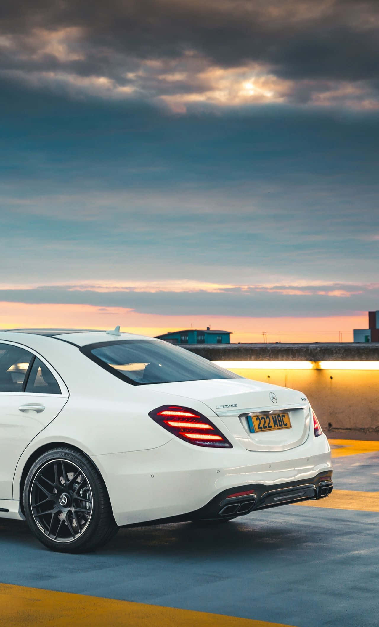 Mercedes 桌布 壁紙 — 一輛白色賓士S-Class轎車在日落時停泊在屋頂上，背景有戲劇性的雲層和溫暖的環境燈光。