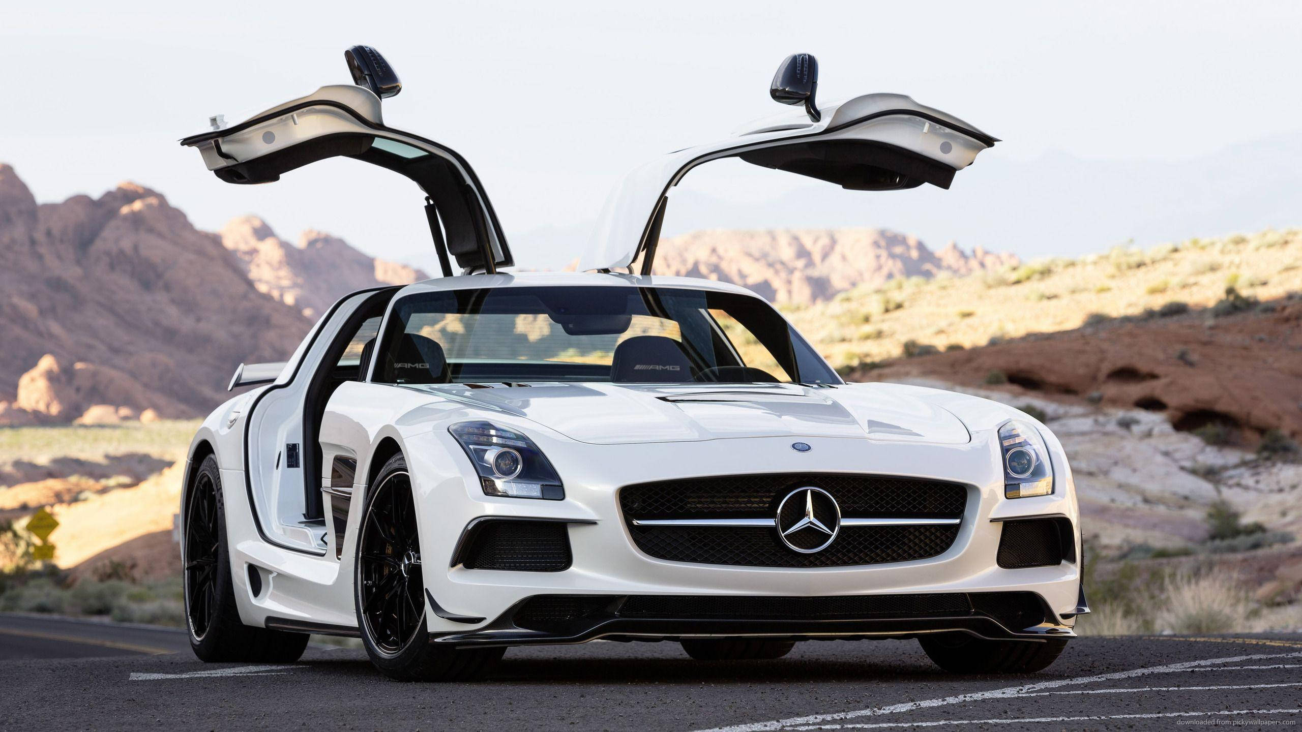 Mercedes Benz Amg 桌布 壁紙 — 一輛白色賓士SLS AMG跑車，鷗翼車門打開，停放在岩石地形的沙漠道路上。
