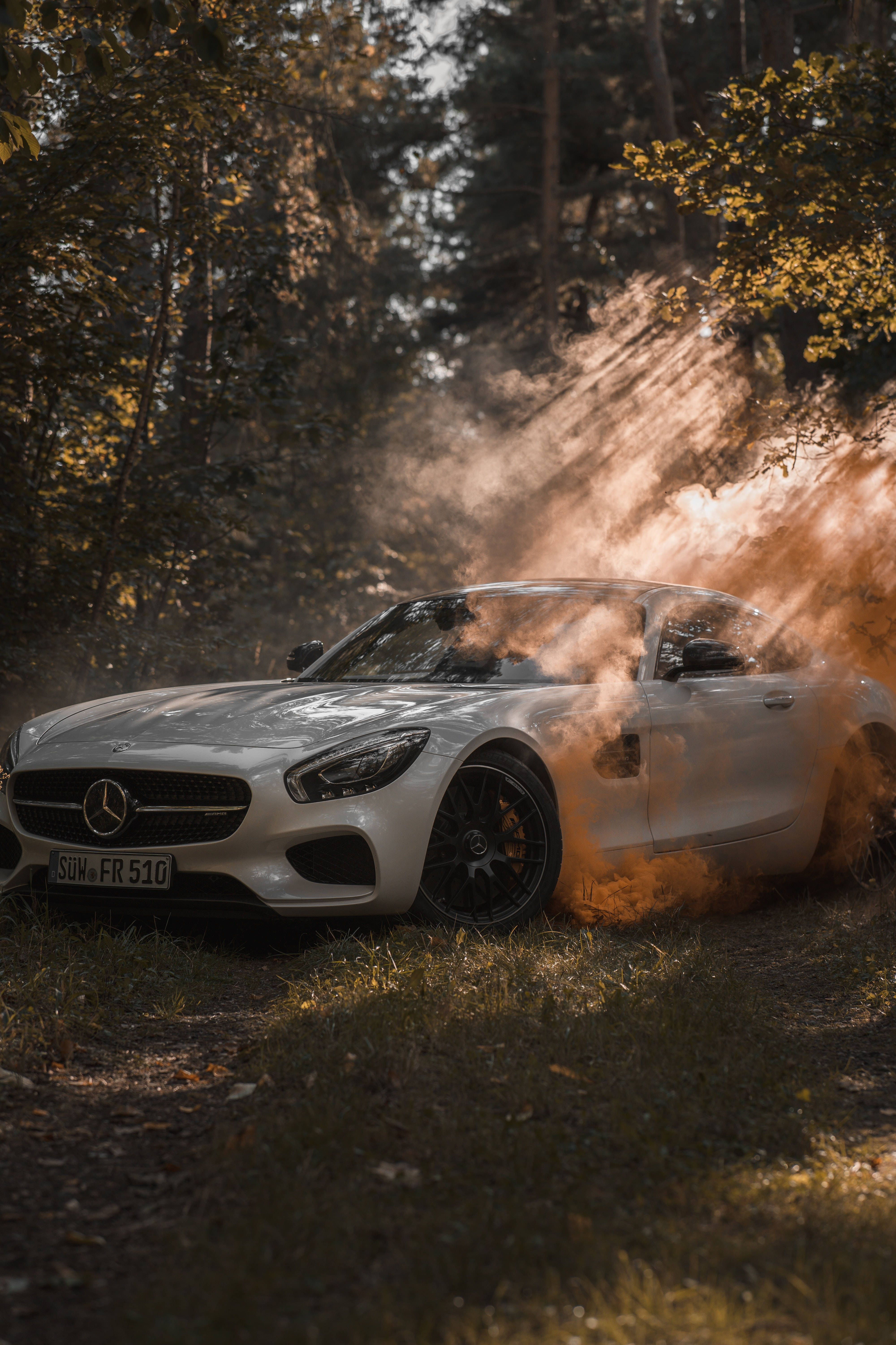 mercedes amg iPhone 桌布 壁紙 — 一輛白色賓士跑車在森林中飄移，揚起橙色煙霧，金色陽光穿過秋樹灑下。