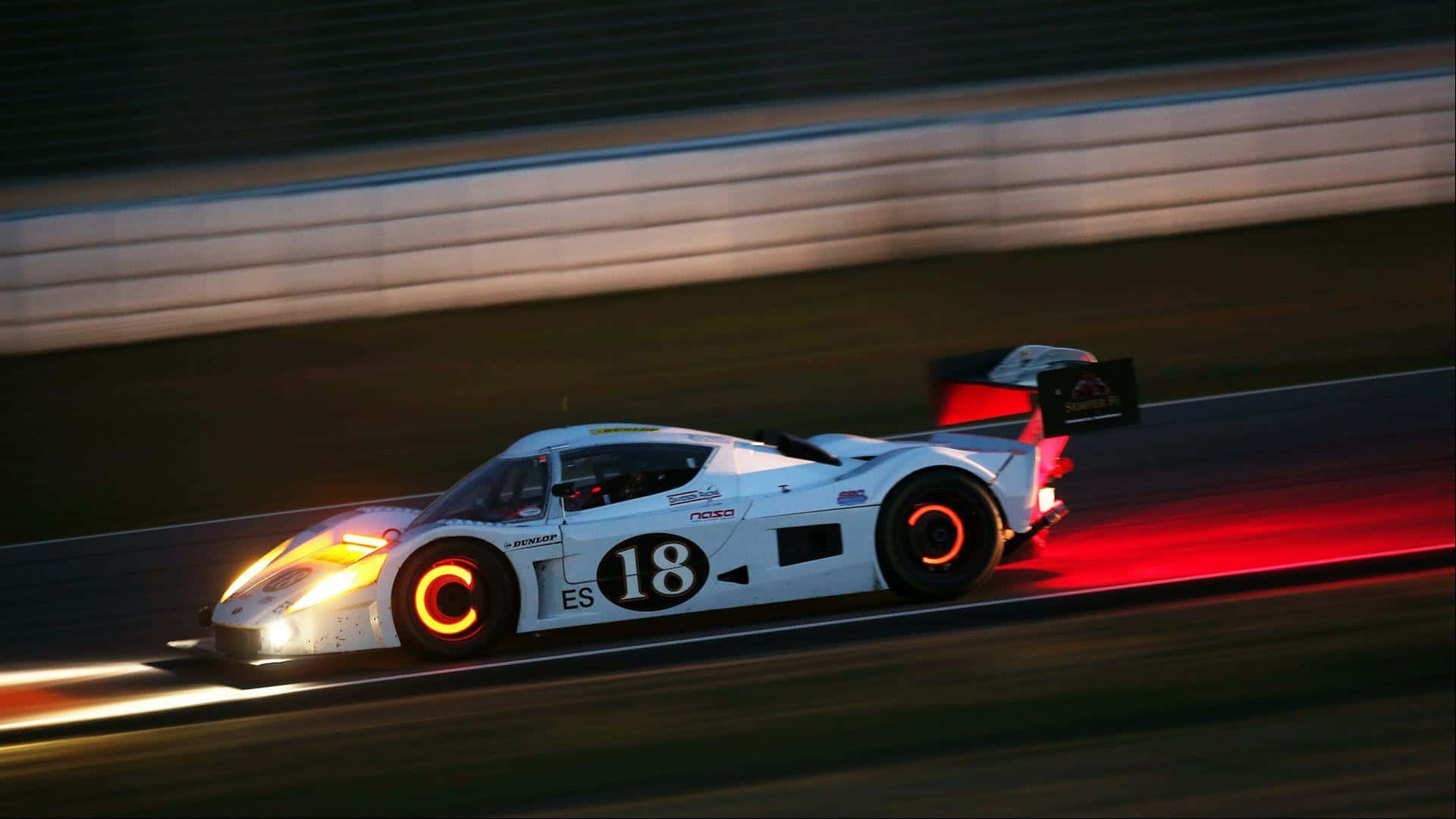 Racing 桌布 壁紙 — 一輛白色賽車，號碼18，在黃昏時分沿著賽道飛馳，留下發光的橙色和紅色光跡。