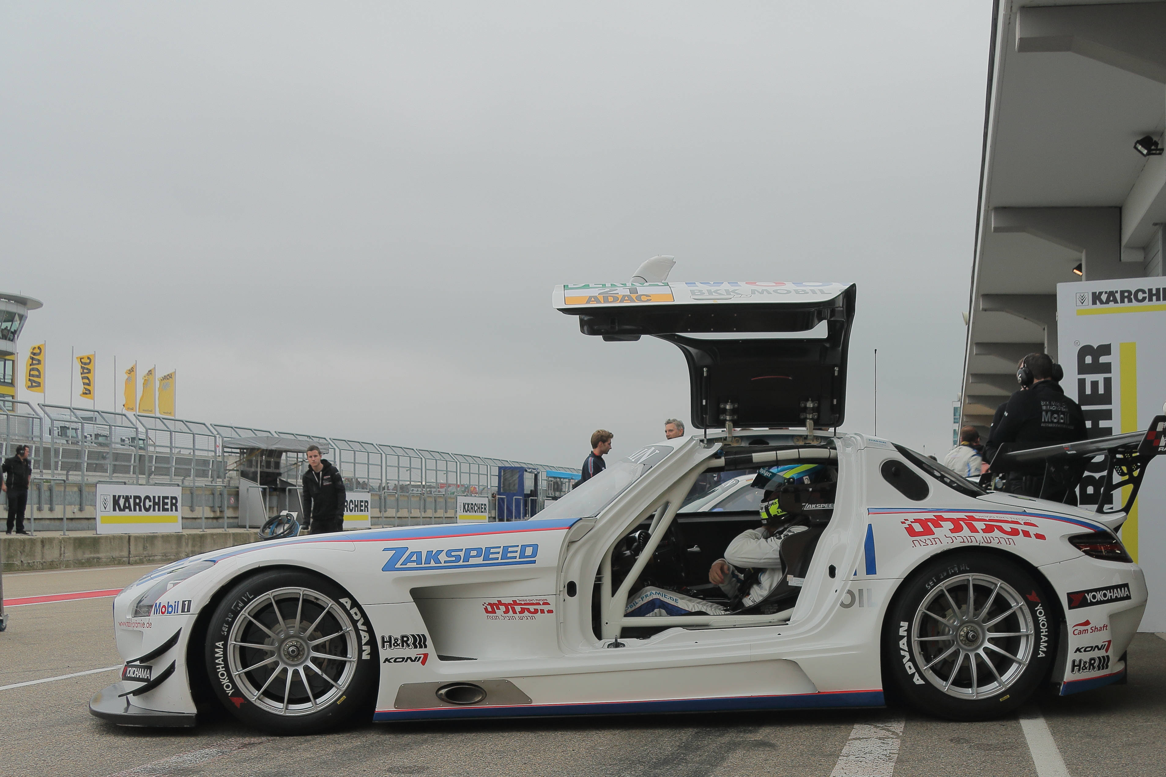 Racing 桌布 壁紙 — 一輛白色賽車打開鷗翼車門停在潮濕的賽道上，戴著頭盔的車手在陰天準備行動。