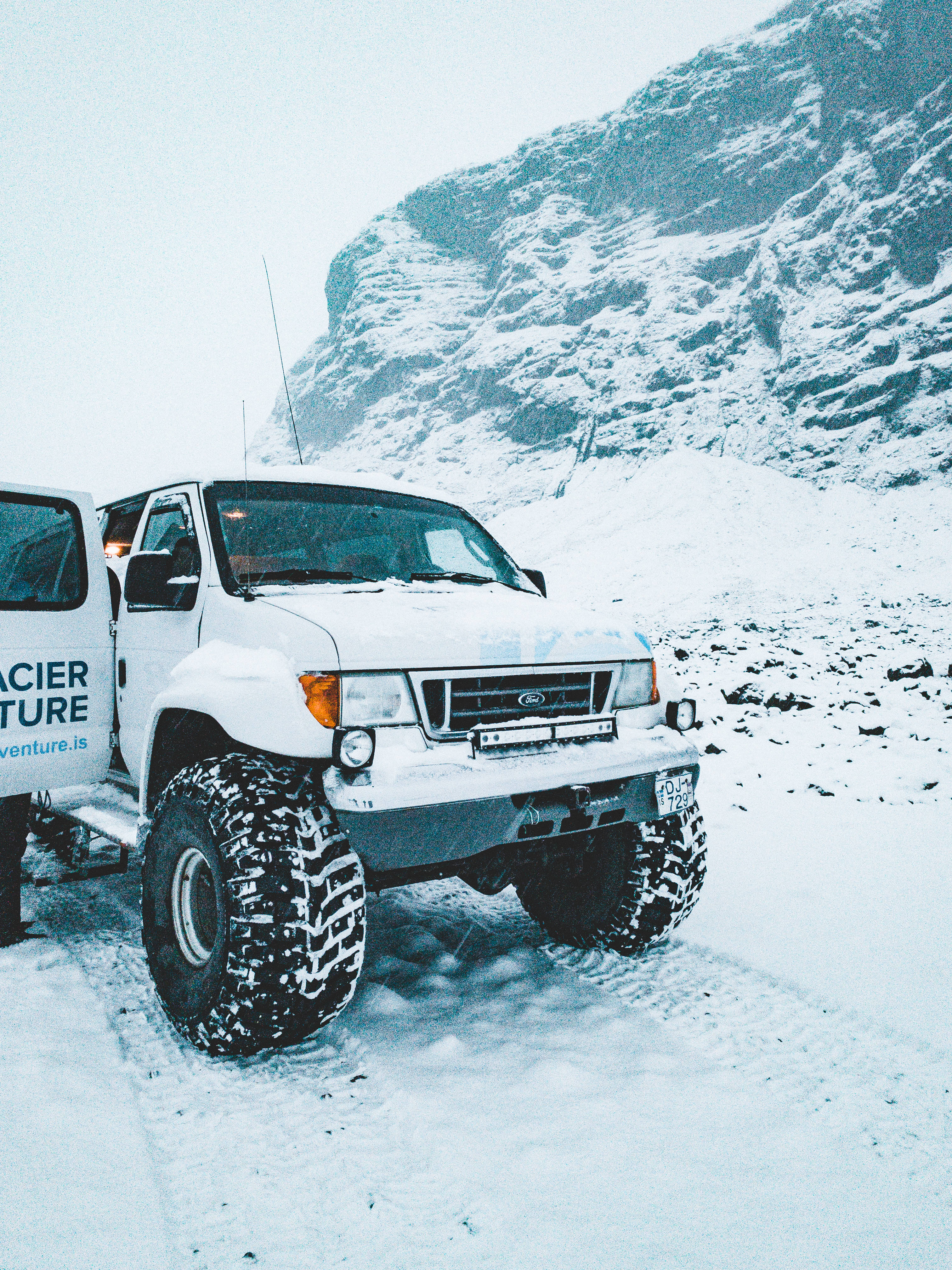 ford iPhone 桌布 壁紙 — 一輛白色越野卡車，輪胎上覆蓋著雪，停在雪地小徑上，旁邊是一座崎嶇、覆蓋著雪的山。