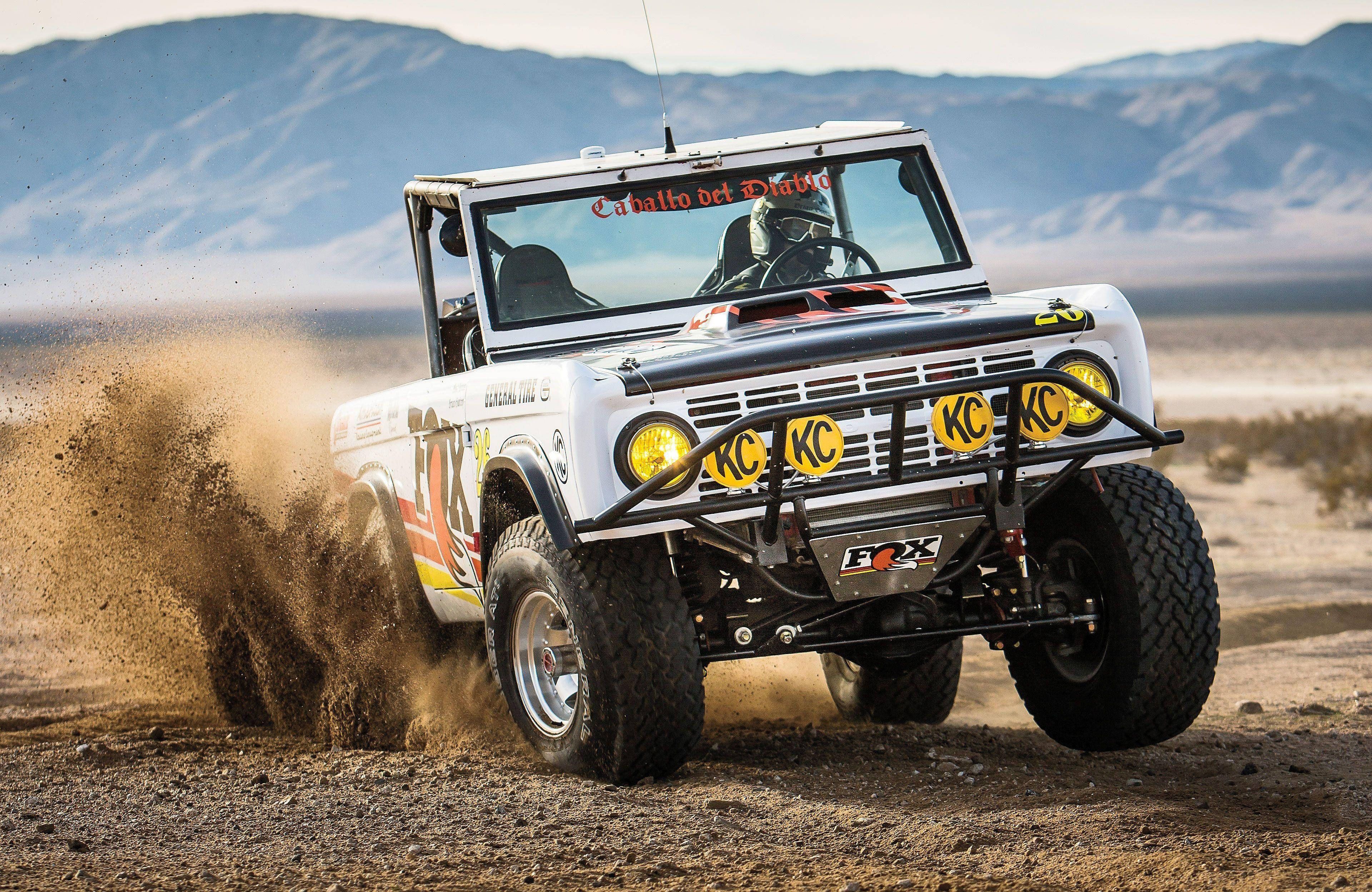 Ford Bronco 桌布 壁紙 — 一輛白色越野車在荒蕪的沙漠中疾馳，揚起塵土，背景是山脈。