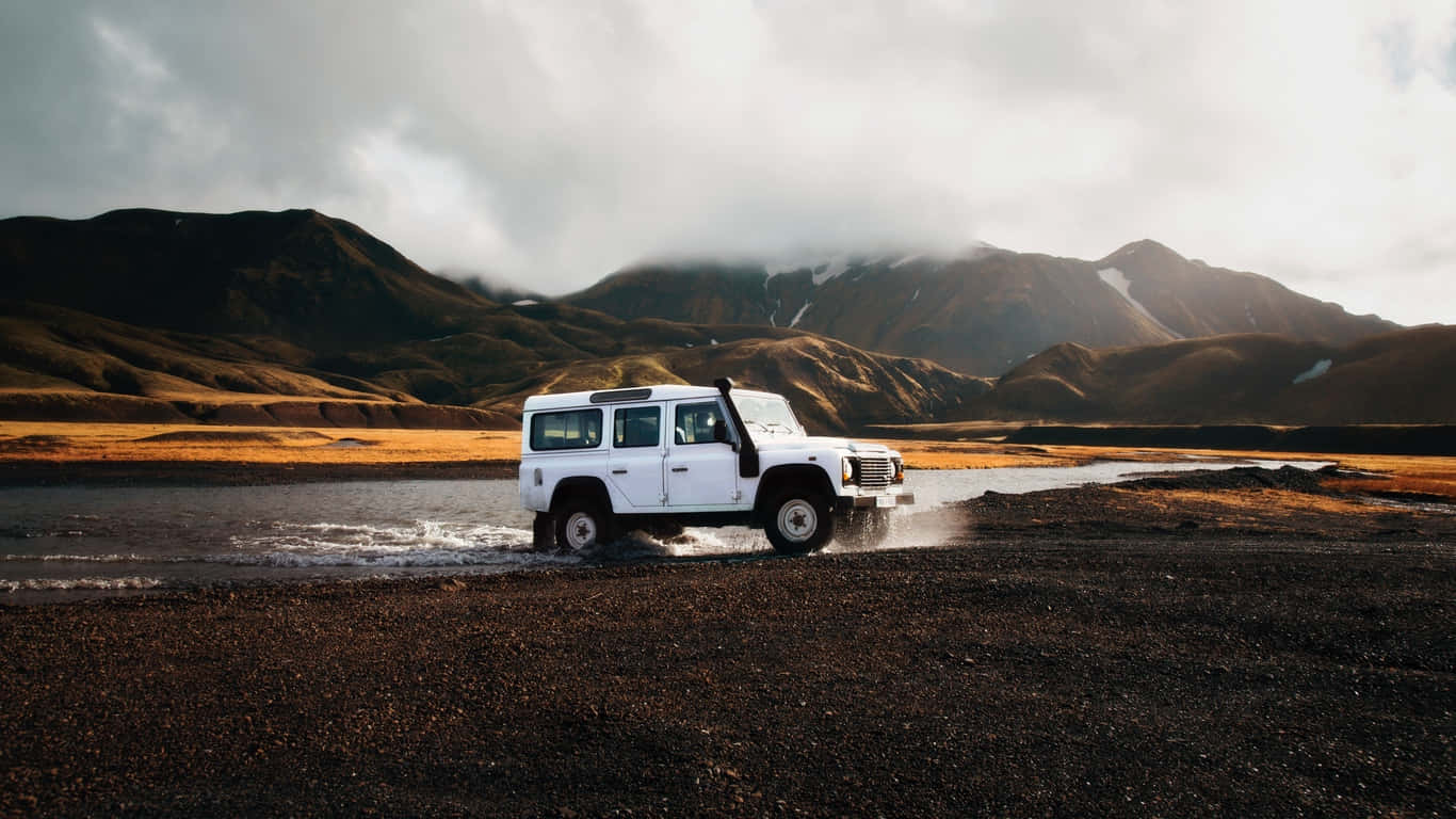 Traveler 桌布 壁紙 — 一輛白色越野車在陰天背景下，濺起水花穿過淺溪，背景是霧氣繚繞的山巒。