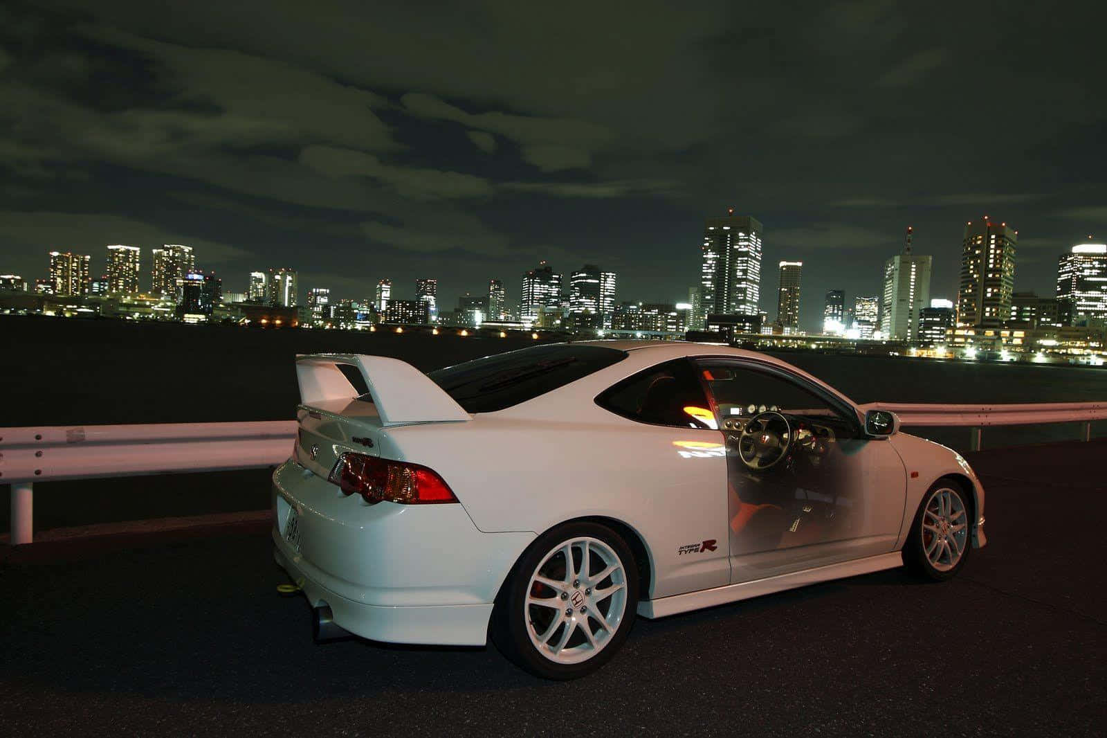 Acura Integra 桌布 壁紙 — 一輛白色跑車在夜間停放，背景是發光的城市天際線。