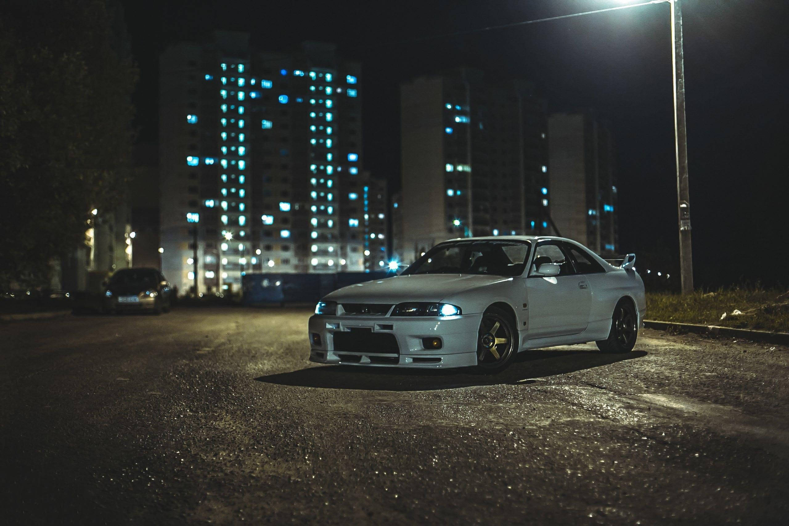 Gtr 桌布 壁紙 — 一輛白色跑車在夜間濕漉漉的城市街道上，在路燈下閃閃發光，背景是發光的藍色公寓大樓。