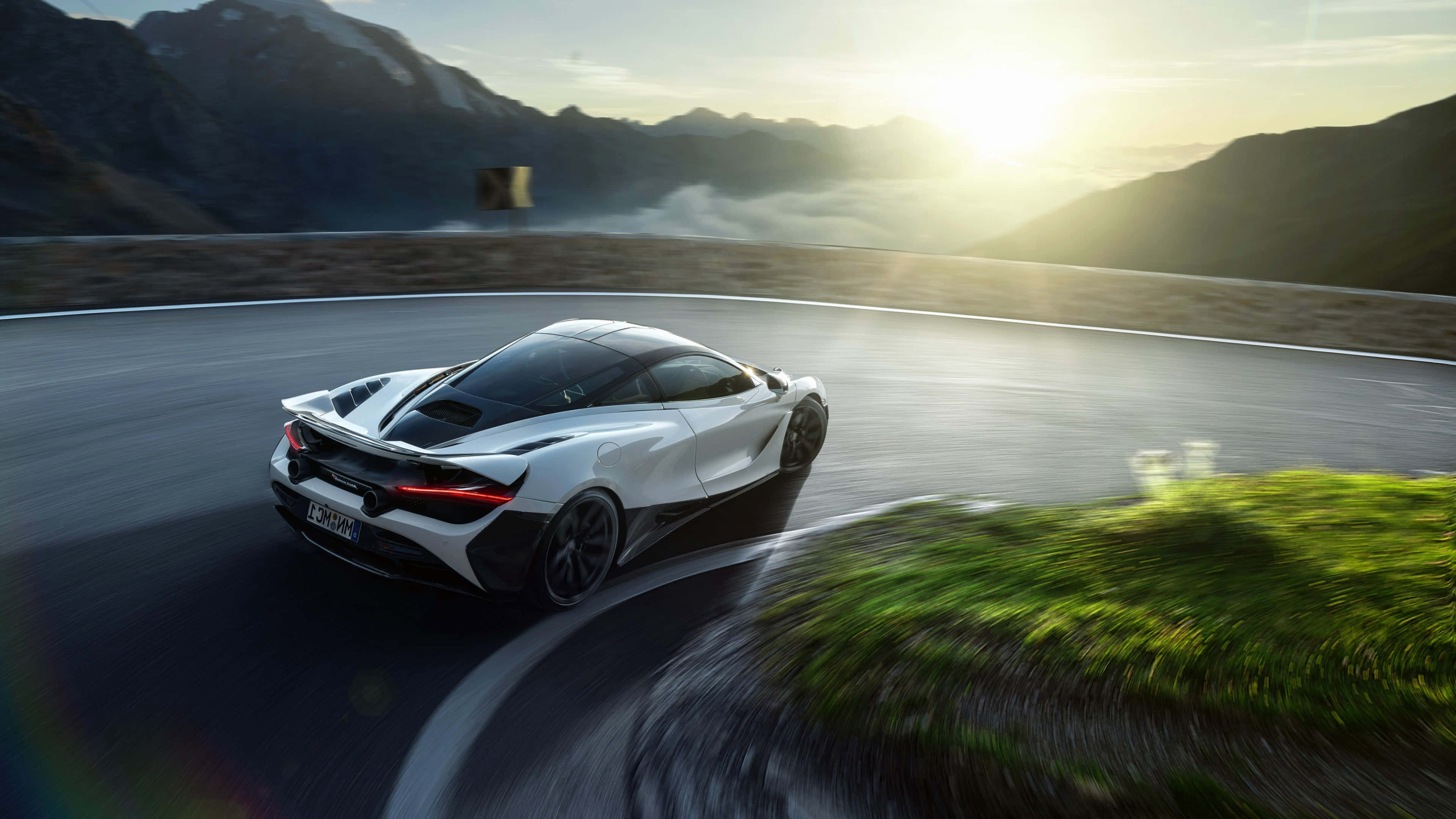 4K Mclaren 720s 桌布 壁紙 — 一輛白色跑車在日出時沿著蜿蜒的山路疾馳，周圍是霧氣繚繞的山峰和充滿活力的綠色植物。