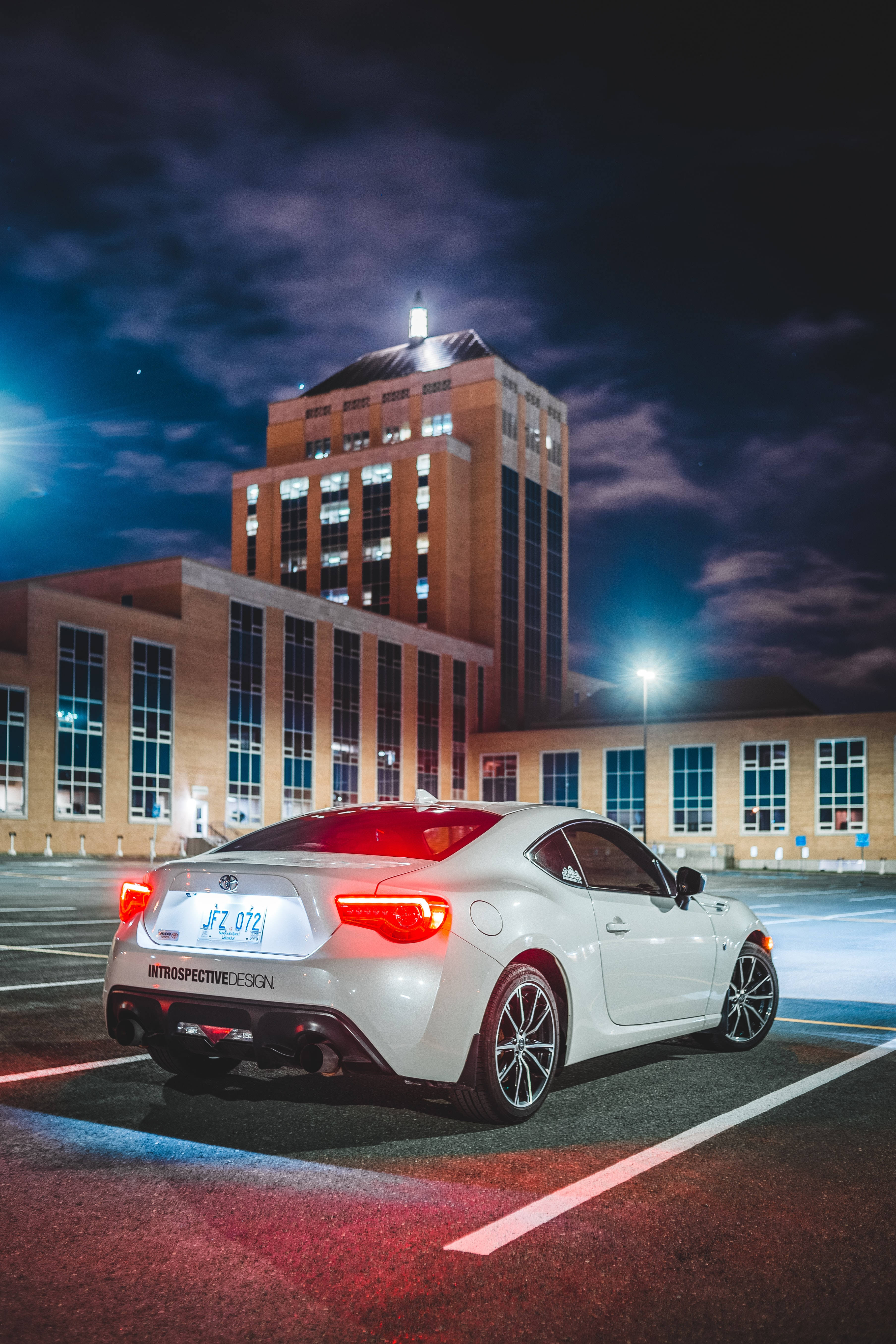 Toyota 桌布 壁紙 — 一輛白色跑車在星空下，停在燈火通明的磚砌建築前，紅色尾燈閃爍。