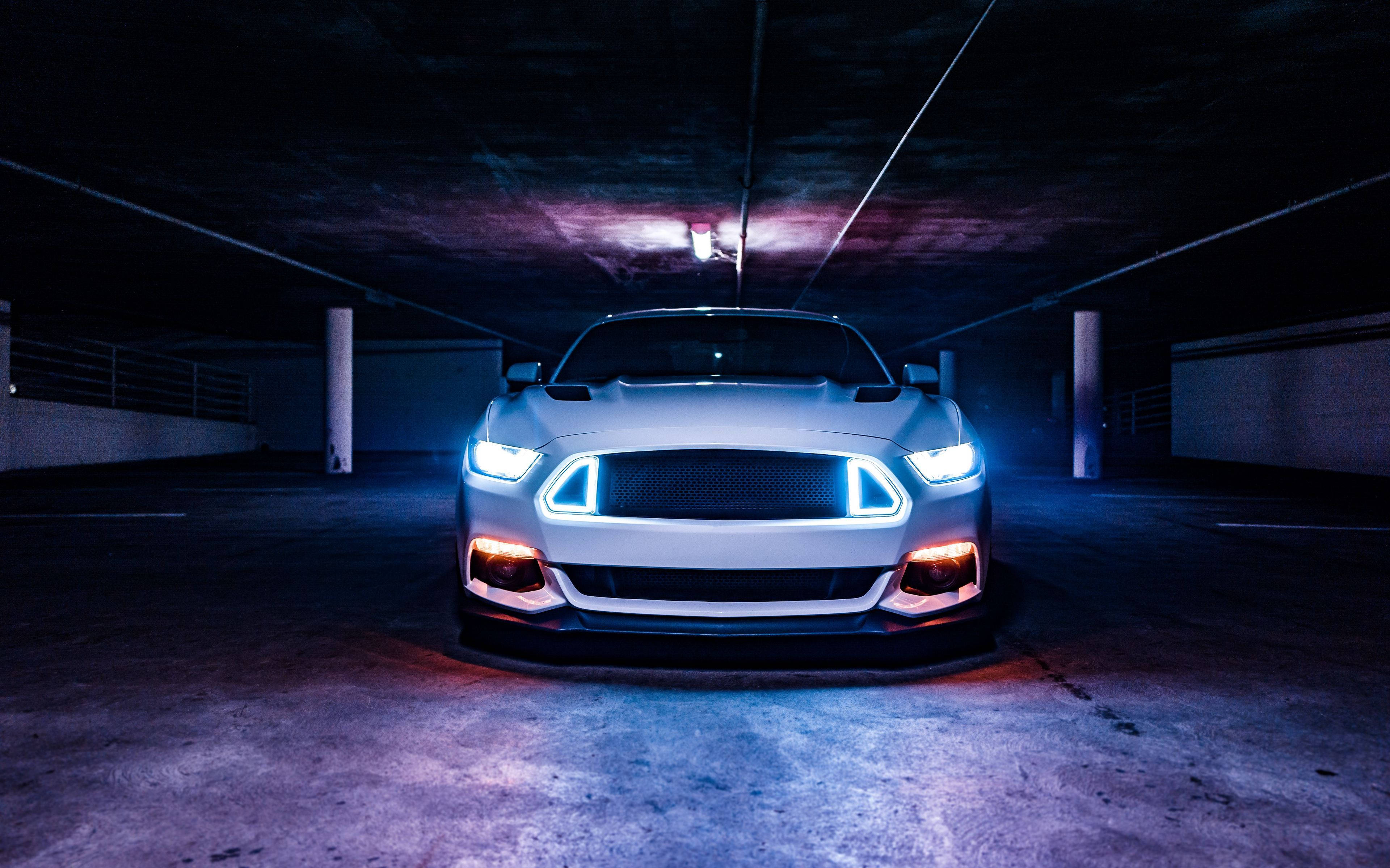 mustang HD 桌布 壁紙 — 一輛白色跑車帶有發光的藍色和橙色車頭燈，主導著光線昏暗的地下停車場。