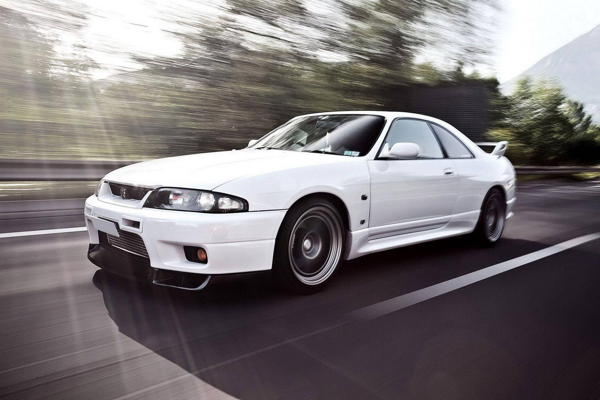 Gtr 桌布 壁紙 — 一輛白色跑車沿著山路飛馳，背景是模糊的綠樹和遠處的山峰。