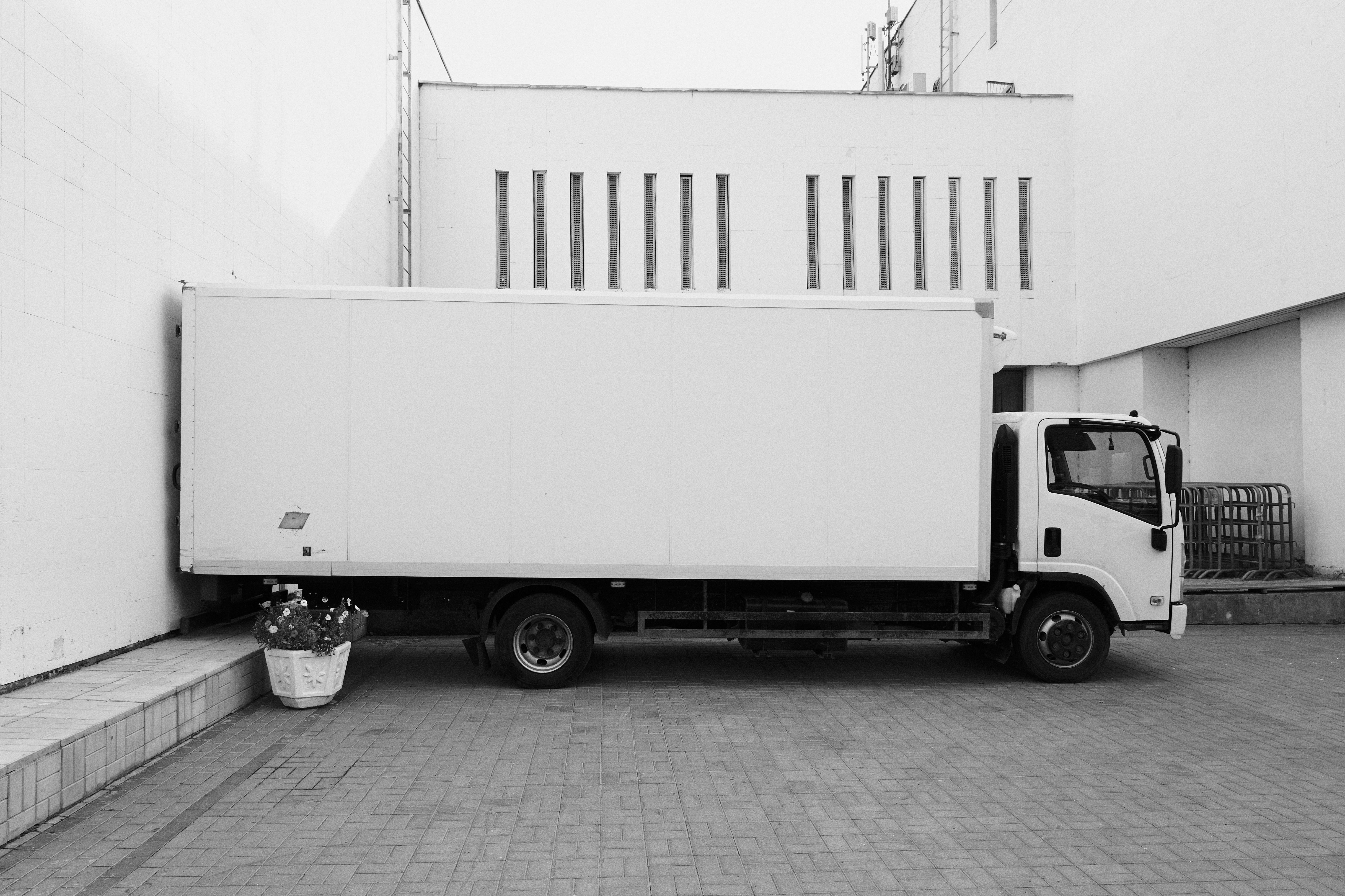 Moving 桌布 壁紙 — 一輛白色送貨車停在一棟現代建築旁邊，建築有垂直窗戶，附近有一盆盆栽植物。