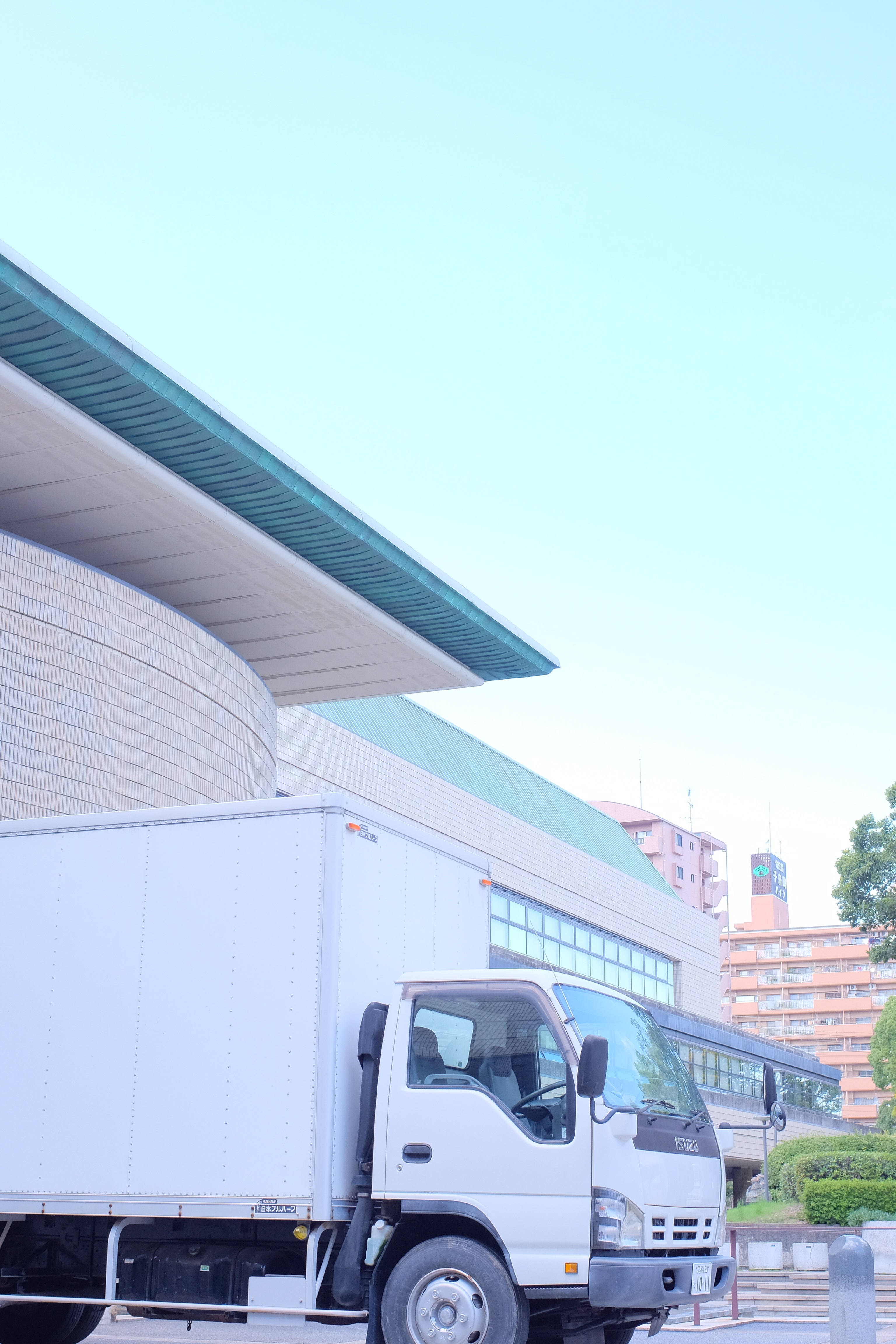 Truck 桌布 壁紙 — 一輛白色送貨車停泊在現代曲線建築下，建築帶有青綠色點綴，背景是晴朗的藍天。