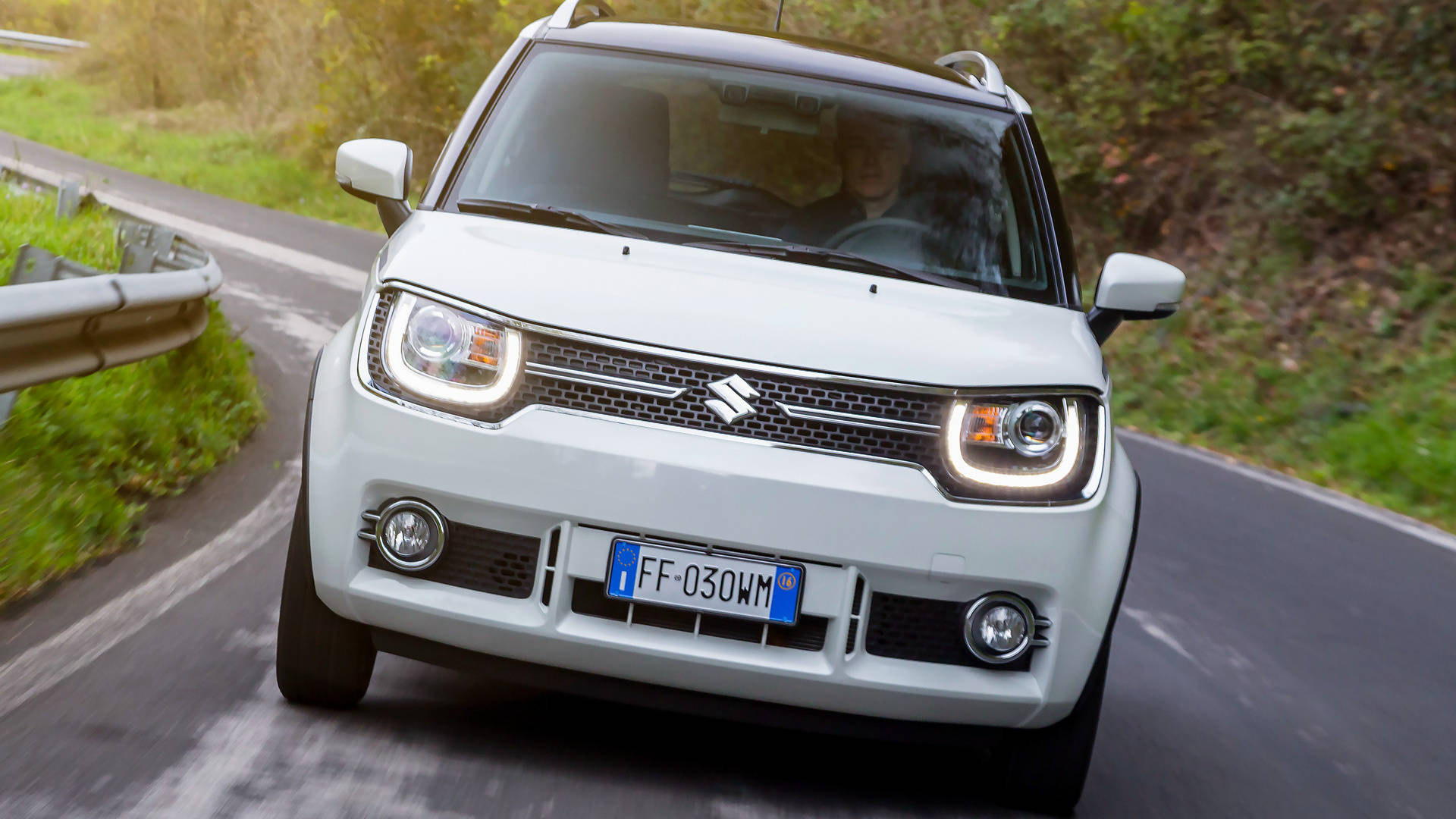 Suzuki 桌布 壁紙 — 一輛白色鈴木 Jimny 沿著蜿蜒的山路行駛，兩旁有綠色植物和護欄。
