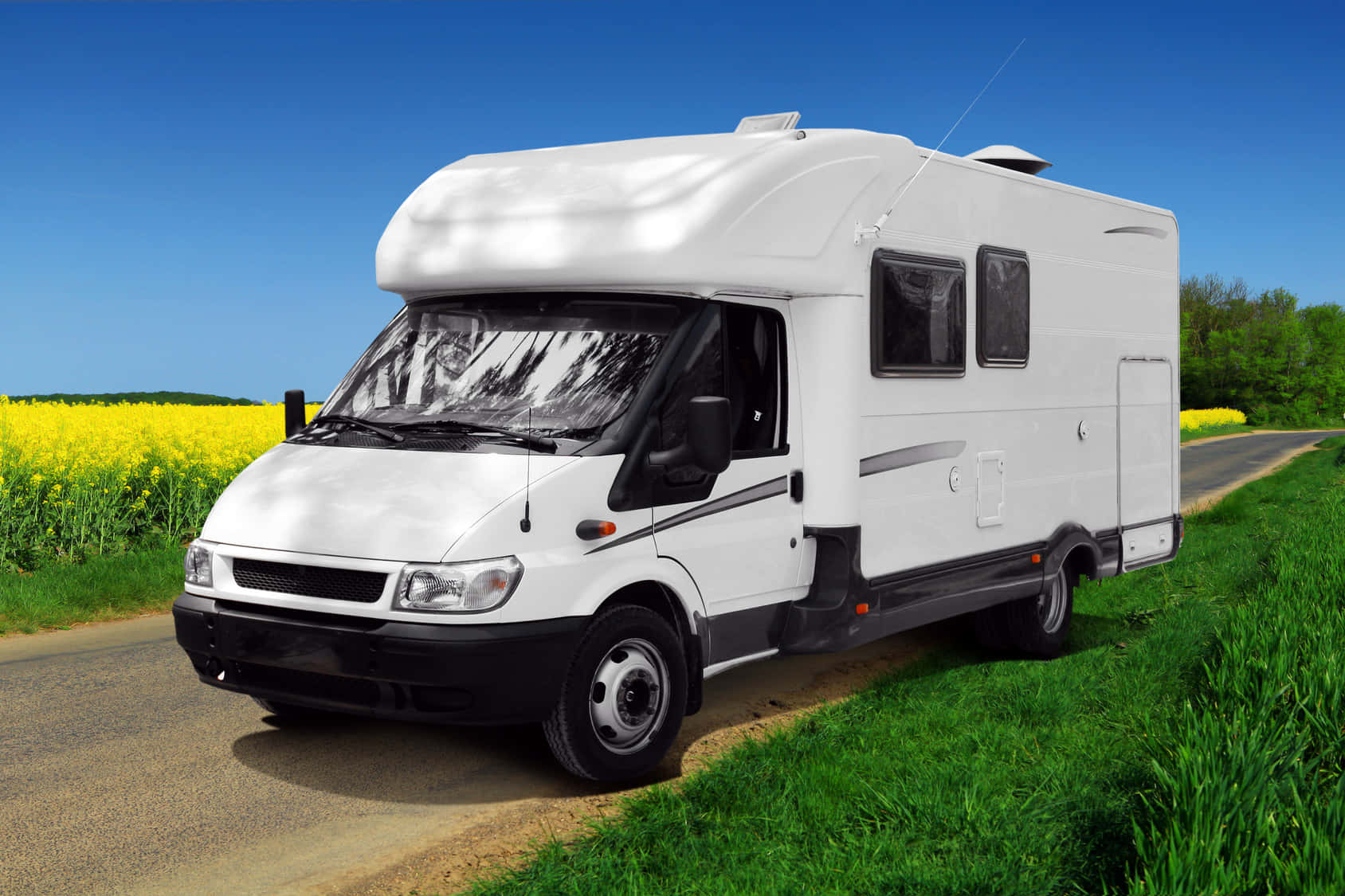 Caravan 桌布 壁紙 — 一輛白色露營車停泊在鄉村道路上，旁邊是充滿活力的黃色油菜花田，天空清澈湛藍。