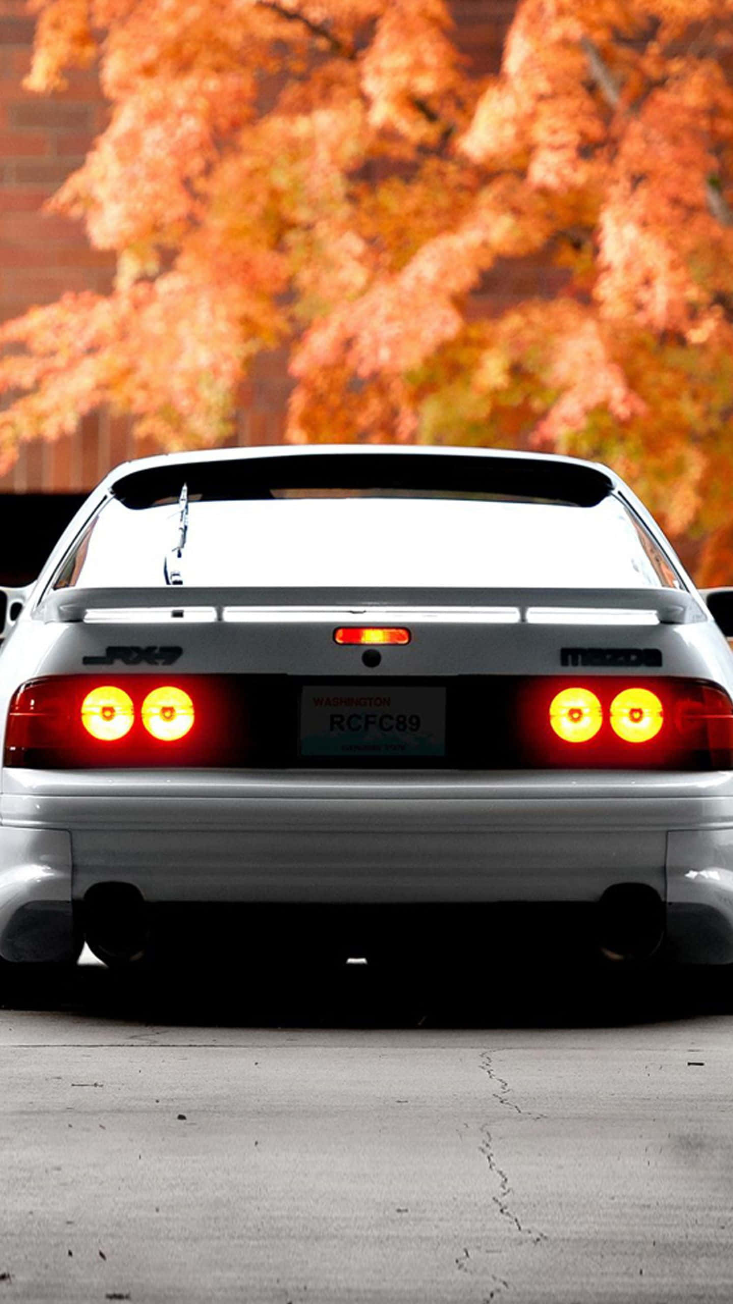 Mazda 桌布 壁紙 — 一輛白色馬自達RX-7跑車，紅色尾燈發光，停放在鮮豔的橙色秋樹下。