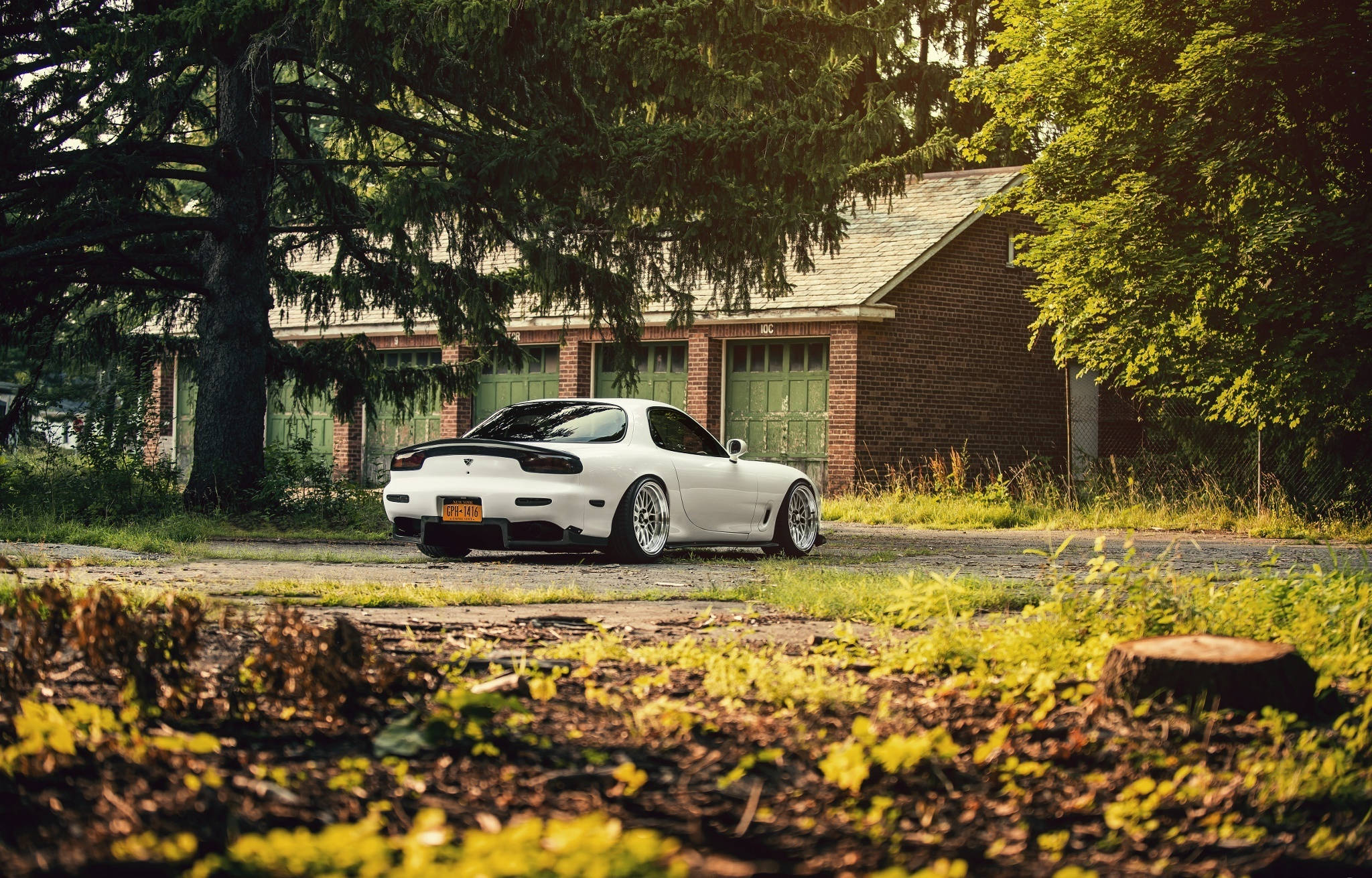 Mazda 桌布 壁紙 — 一輛白色馬自達RX-7跑車停放在磚房前的碎石車道上，周圍環繞著茂密的綠樹。
