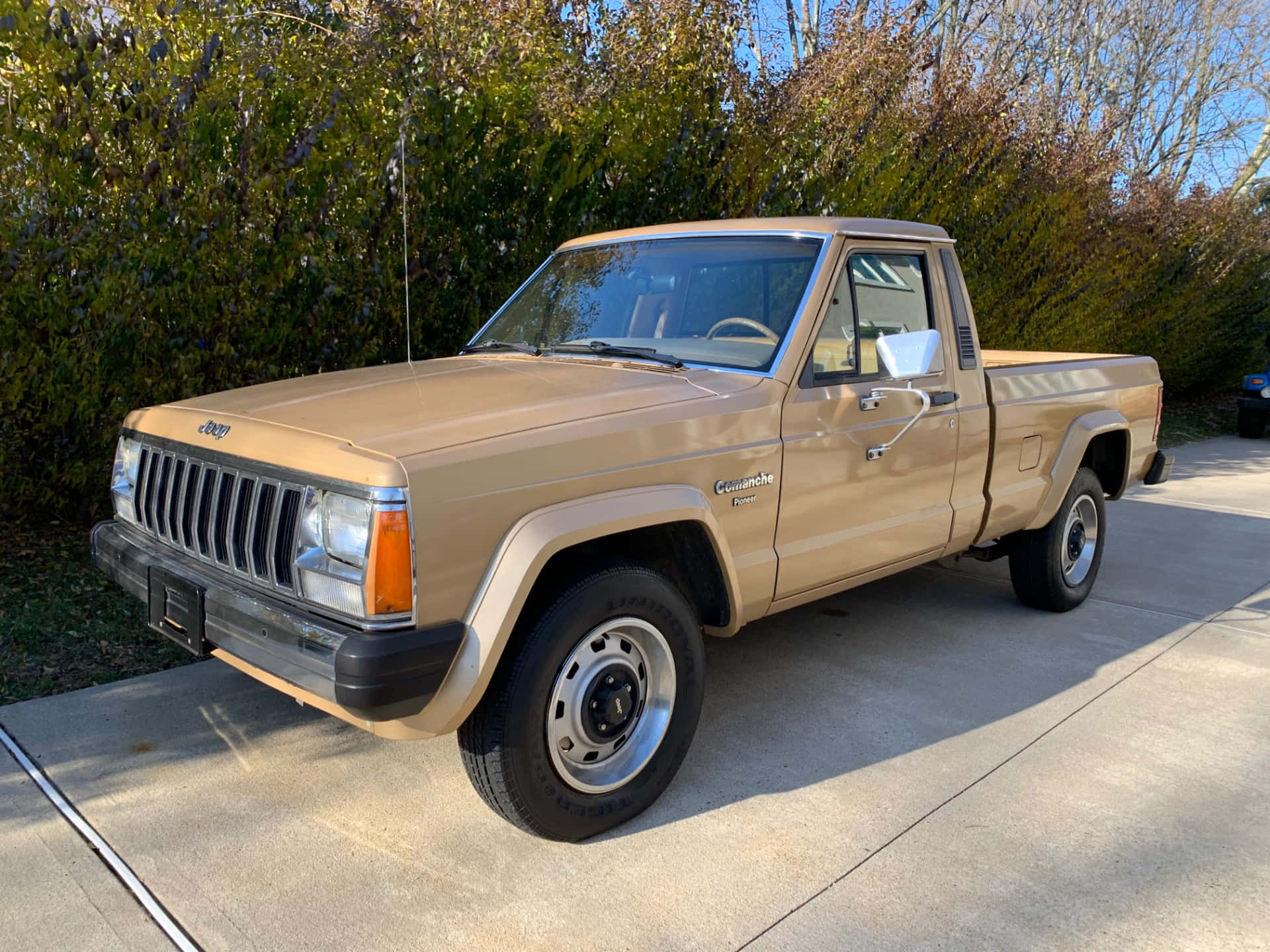 Jeep Comanche 桌布 壁紙 — 一輛米色1980年代Jeep Comanche皮卡車停在混凝土車道上，背景有秋樹。