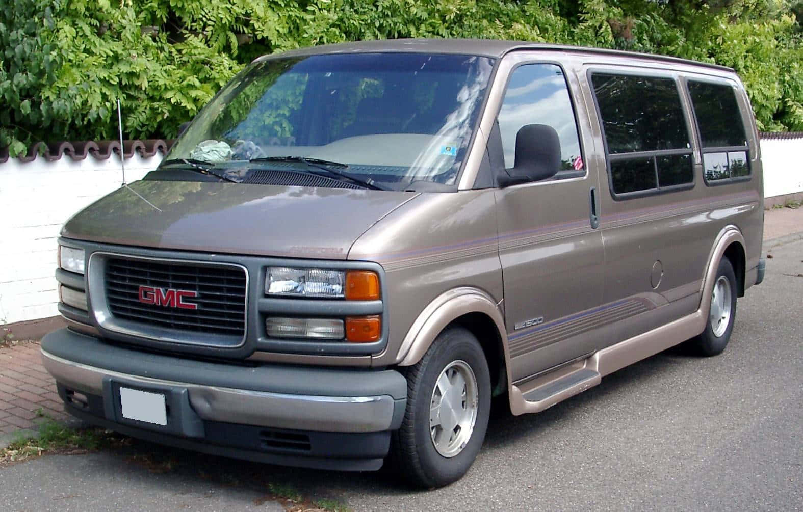 Gmc Savana 桌布 壁紙 — 一輛米色GMC Safari小型貨車停在鋪砌的車道上，旁邊有白色圍欄和茂密的綠色樹葉。