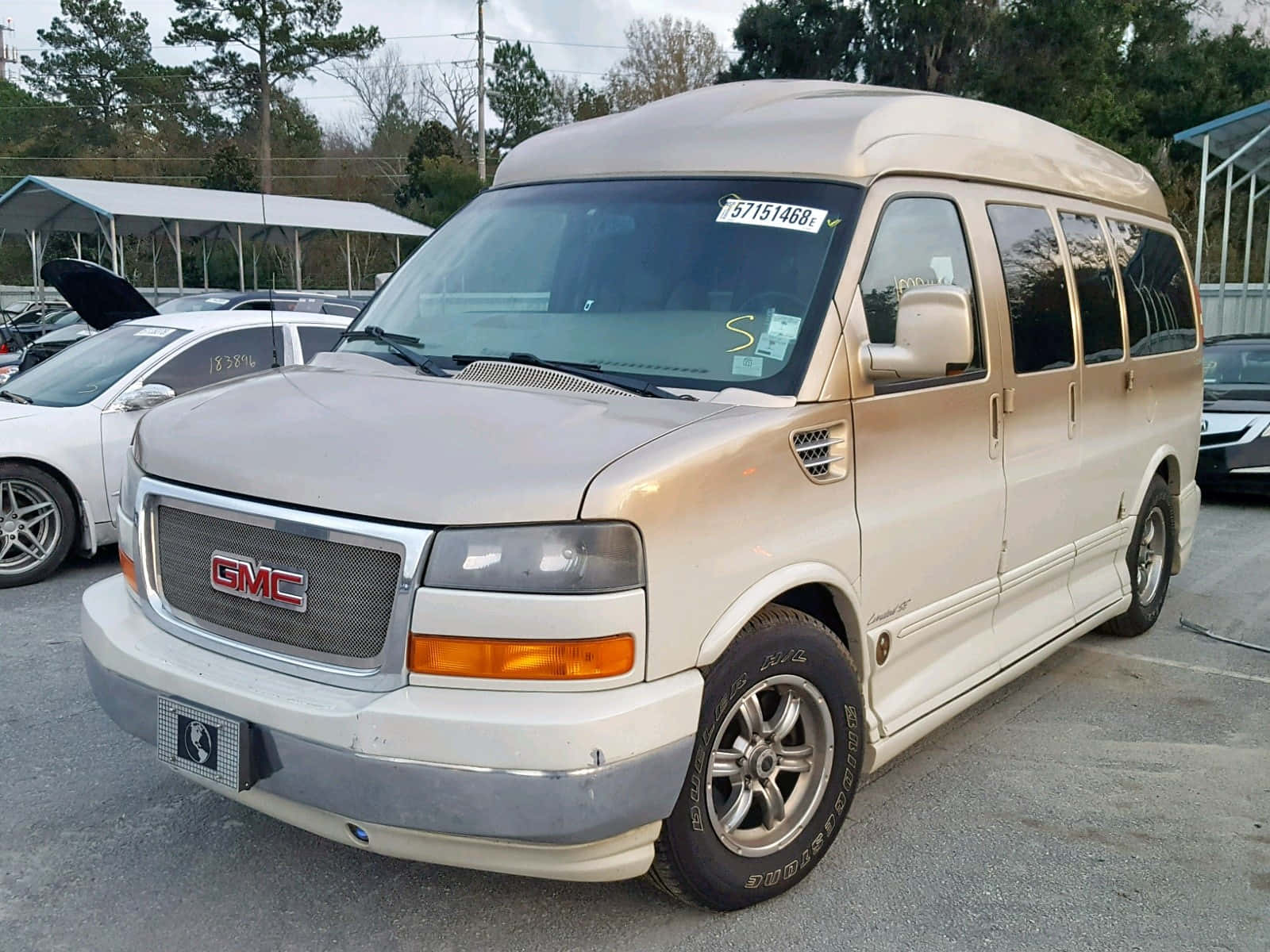 Gmc Savana 桌布 壁紙 — 一輛米色GMC露營車停放在停車場，背景有樹木和其他車輛。