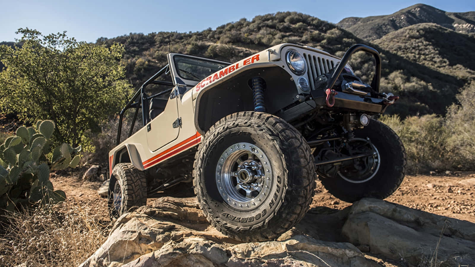 Jeep Cj 桌布 壁紙 — 一輛米色Jeep Scrambler配備超大輪胎，在明亮的日光下征服岩石沙漠地形。