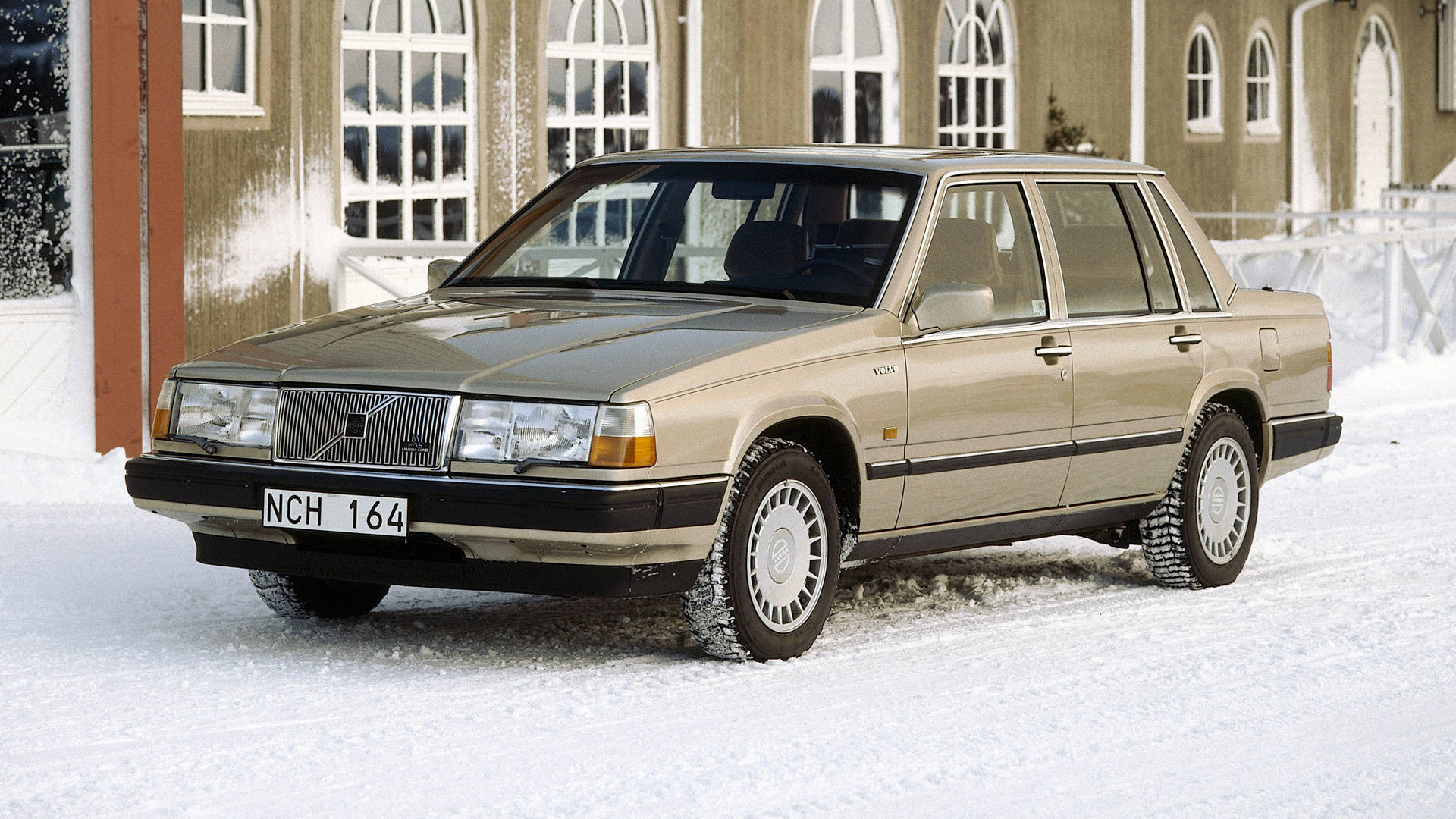 volvo iPhone 桌布 壁紙 — 一輛米色富豪740轎車停在新雪中，前面是木造建築，窗戶有白色邊框。