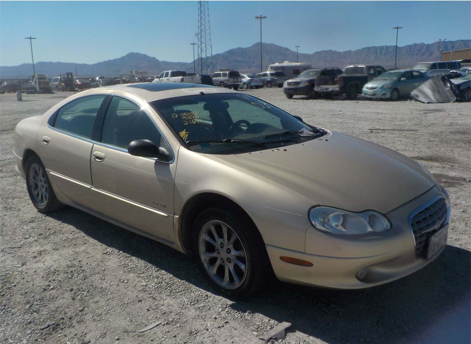 Chrysler Lhs 桌布 壁紙 — 一輛米色轎車停放在陽光明媚的碎石地上，背景有山巒。
