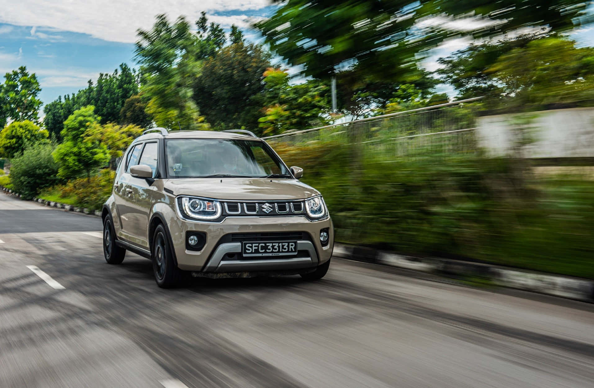 Unorthodox 桌布 壁紙 — 一輛米色鈴木 Jimny SUV 在藍天白雲下，沿著綠樹成蔭的道路疾馳，動態模糊傳達出動感十足的運動感。