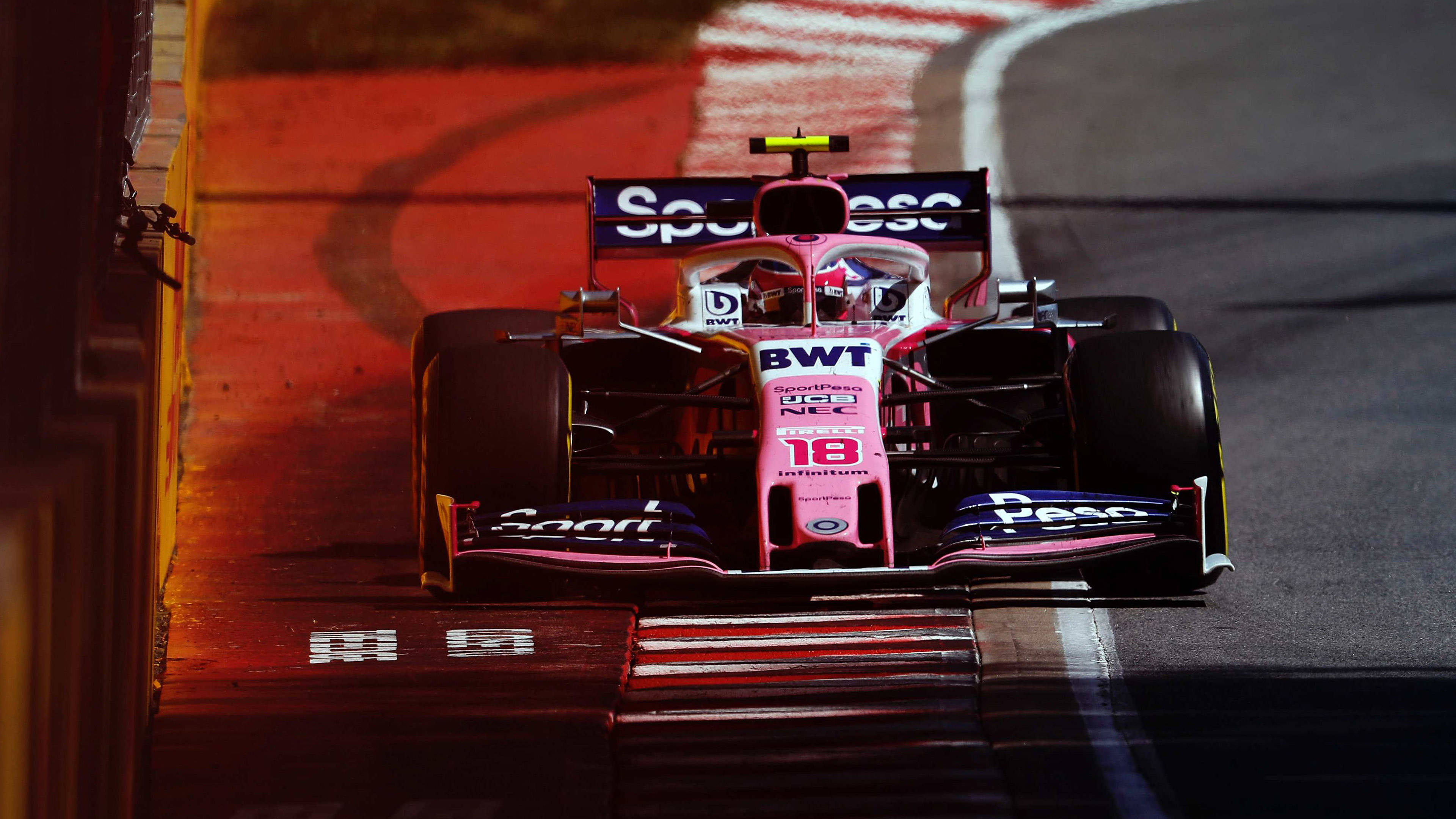 Formula One 桌布 壁紙 — 一輛粉紅色和黑色的 Formula 1 賽車，號碼 18，在夜間於溫暖橙色燈光照亮的賽道上奔馳。