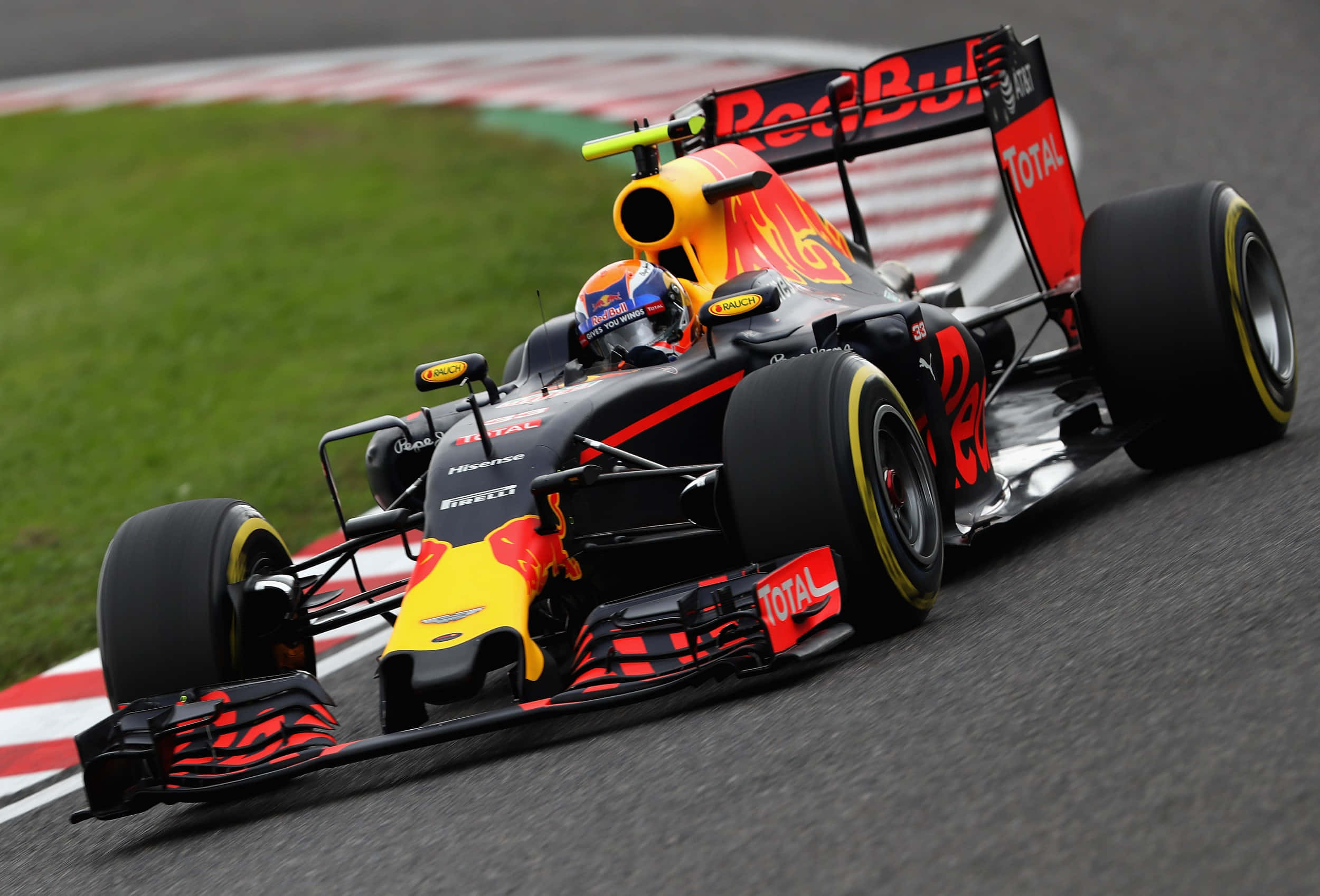 HD F1 2016 桌布 壁紙 — 一輛紅牛一級方程式賽車，帶有鮮豔的紅、黃、黑配色，在賽道彎道上疾馳，背景有綠色草地和紅白路緣石。