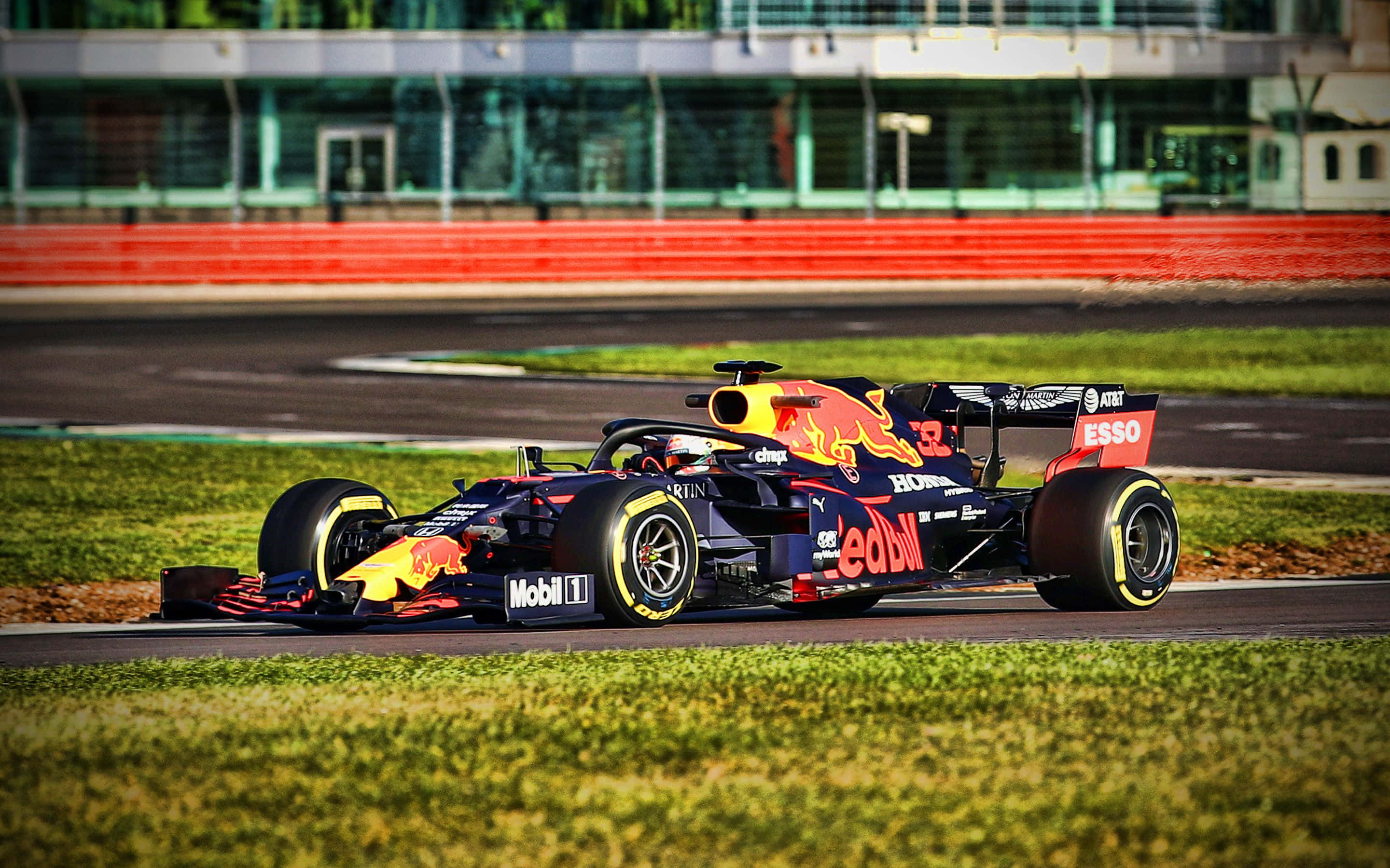 Max Verstappen 桌布 壁紙 — 一輛紅牛一級方程式賽車以鮮豔的黃藍配色在賽道上疾馳，背景是模糊的綠色草地和紅色護欄。
