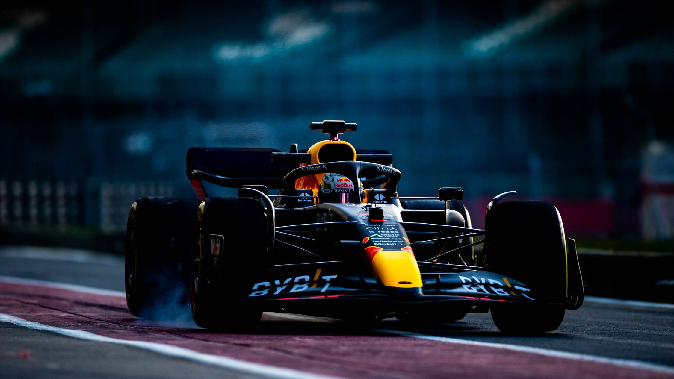 Formula 1 Desktop 桌布 壁紙 — 一輛紅牛一級方程式賽車在夜間光線昏暗的賽道上飄移，輪胎冒出煙霧。
