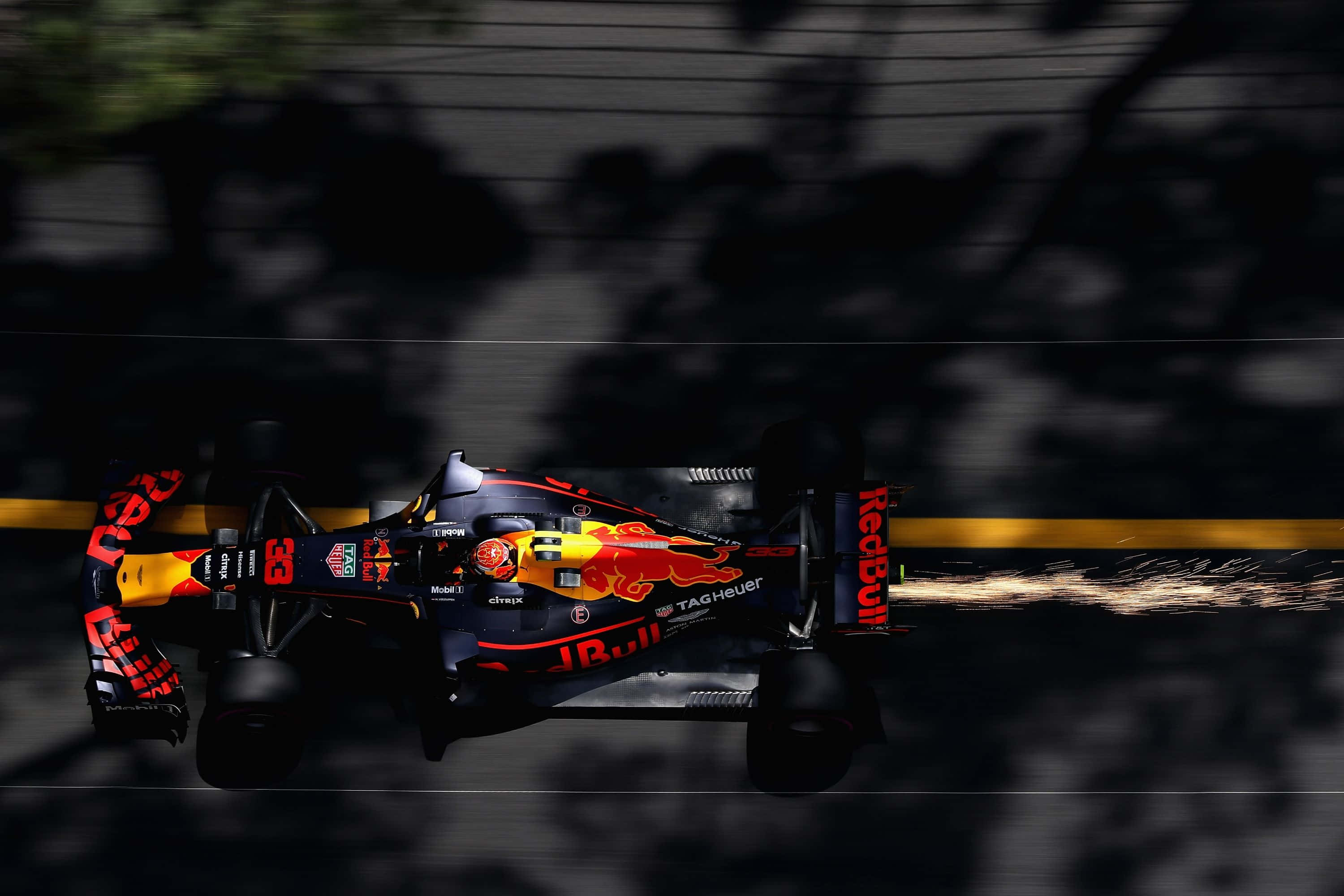 Max Verstappen 桌布 壁紙 — 一輛紅牛一級方程式賽車在樹蔭下高速駛過，帶有動態模糊和輪胎火花。