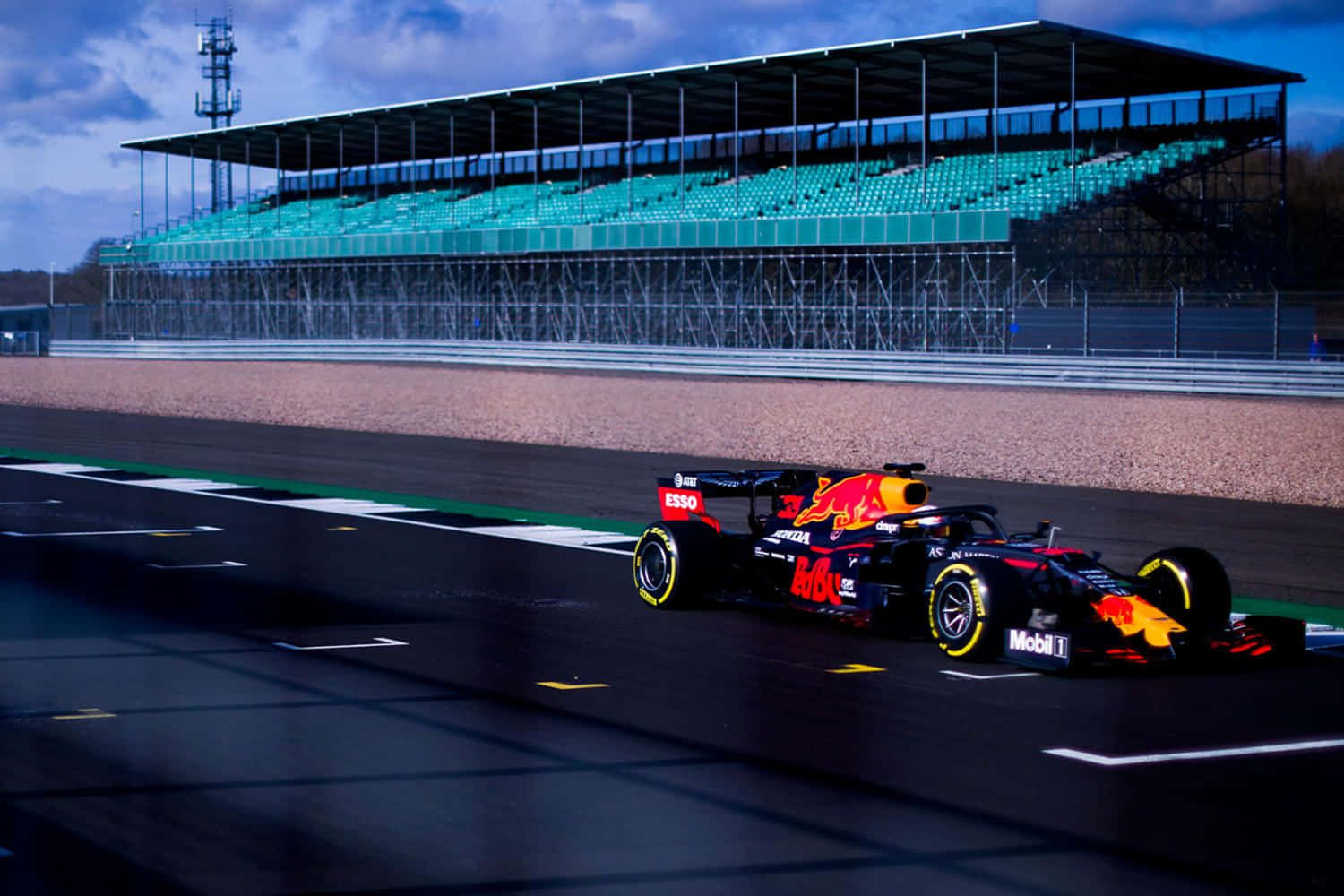 Max Verstappen 桌布 壁紙 — 一輛紅牛一級方程式賽車在潮濕的賽道上疾馳，空無一人的藍綠色看台在陰天之下。