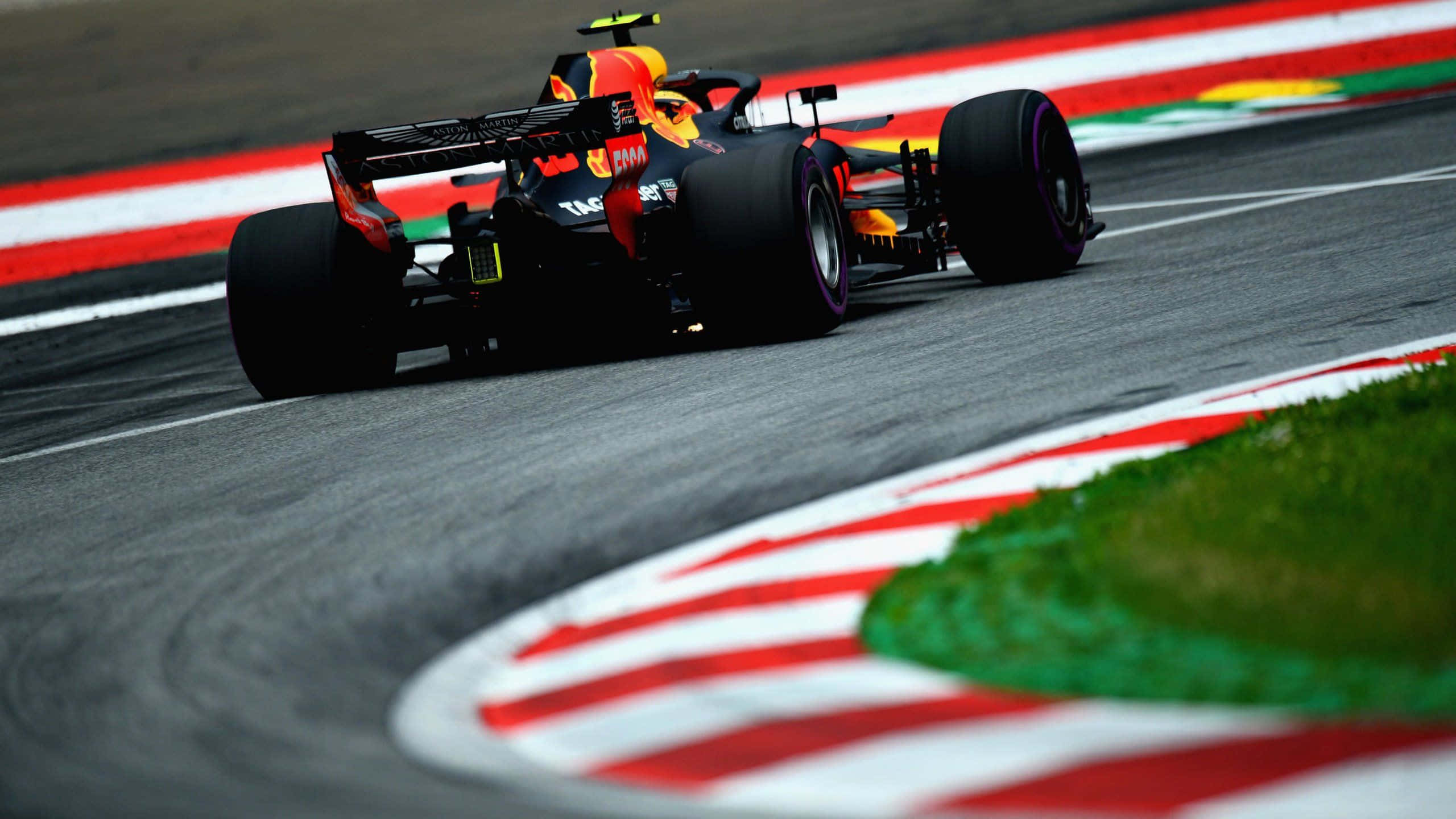 Max Verstappen 桌布 壁紙 — 一輛紅牛一級方程式賽車在賽道上高速駛過一個急彎，賽道邊緣有紅、白、綠三色的路緣石。