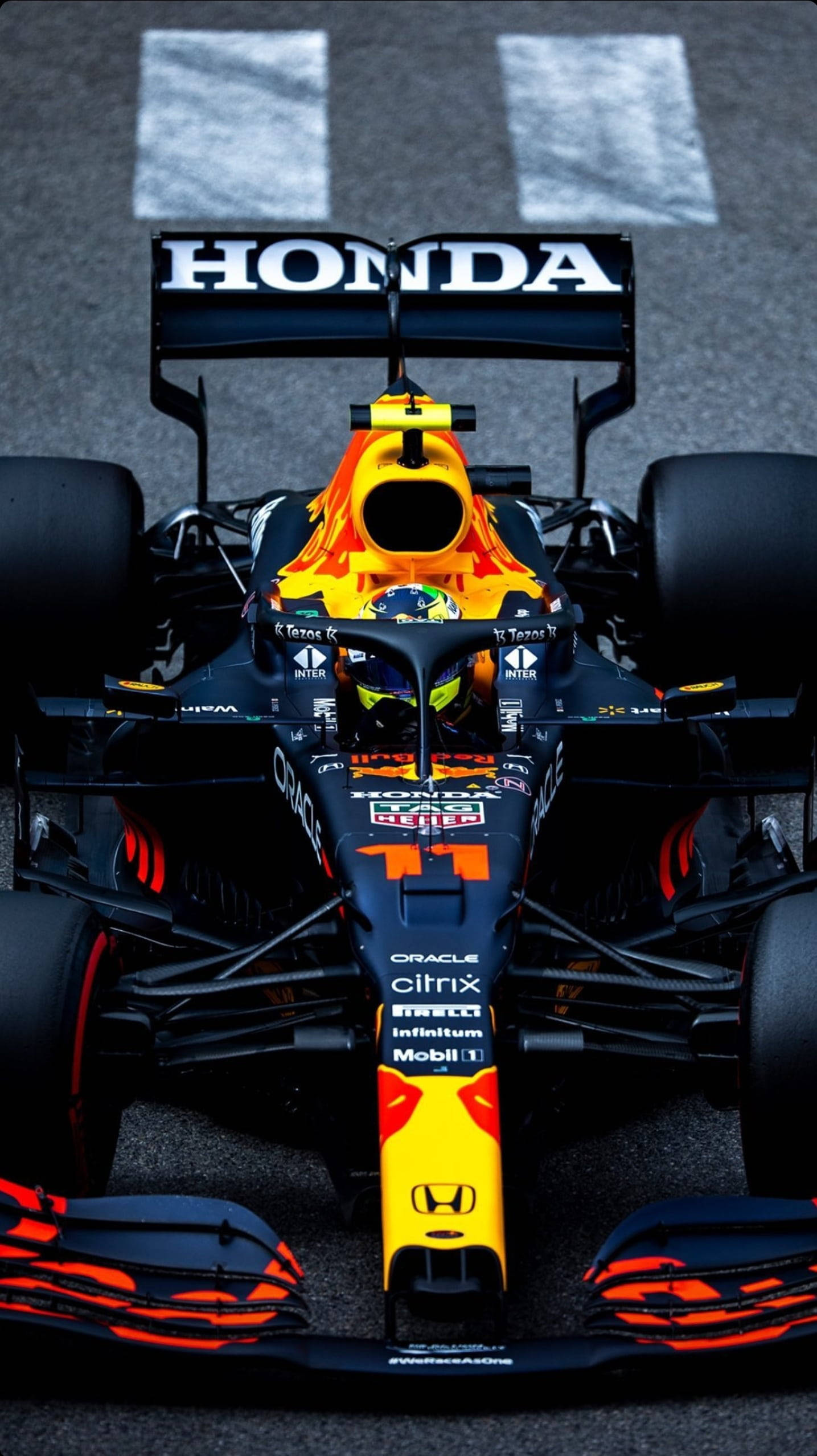 sergio perez 桌布 壁紙 — 一輛紅牛車隊一級方程式賽車，帶有鮮豔的橙色和黑色塗裝，停在賽道發車格上，準備高速競賽。