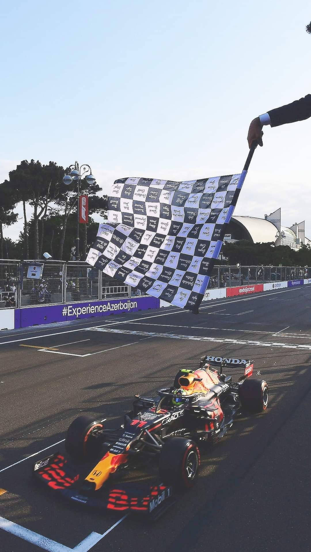 sergio perez 桌布 壁紙 — 一輛紅牛車隊一級方程式賽車在巴庫城市賽道越過終點線，同時一名賽事官員揮動方格旗。