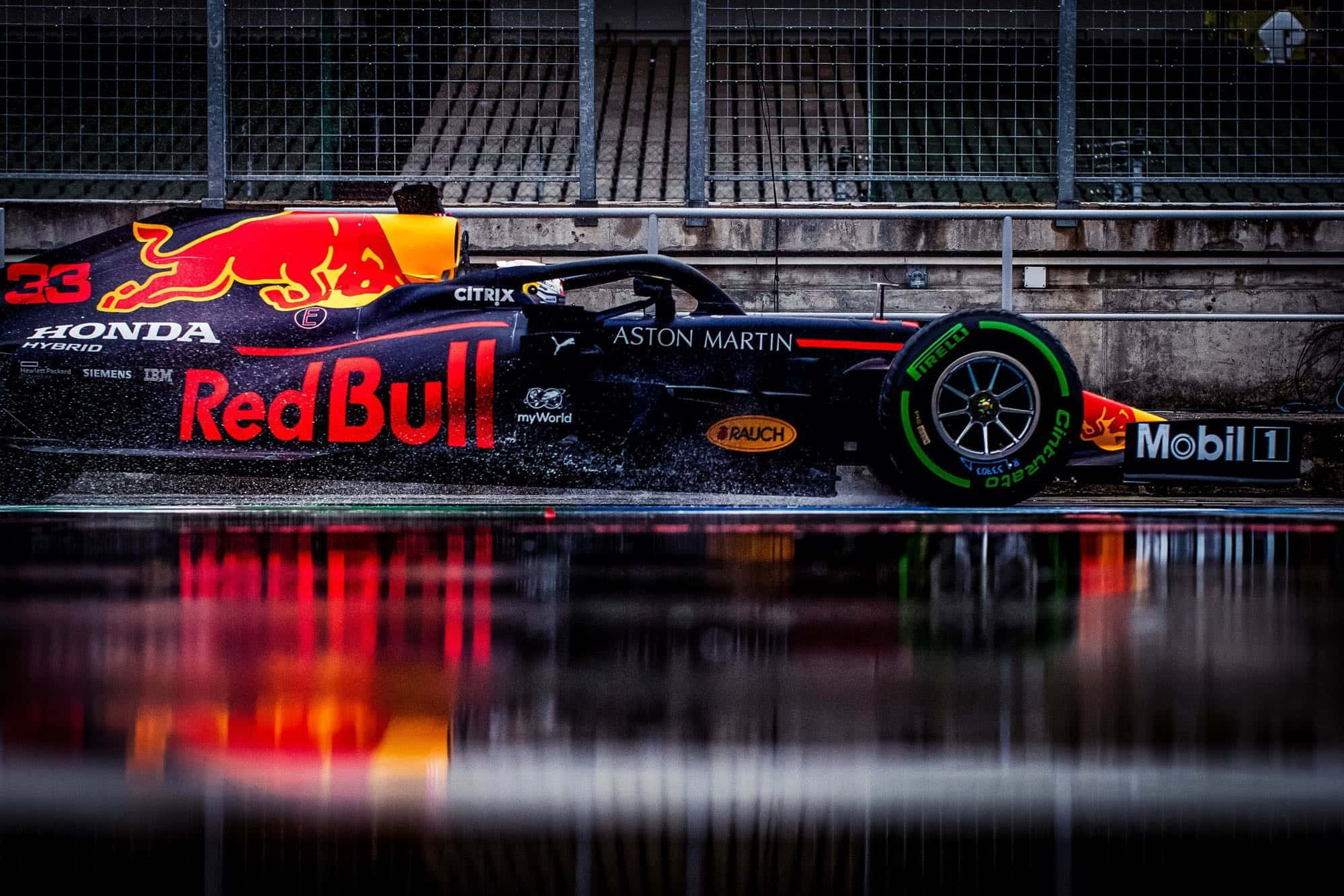 Formula One 桌布 壁紙 — 一輛紅牛車隊一級方程式賽車在潮濕賽道的水坑中飛馳，水花四濺，倒映出陰天天空下鮮明的贊助商標誌。