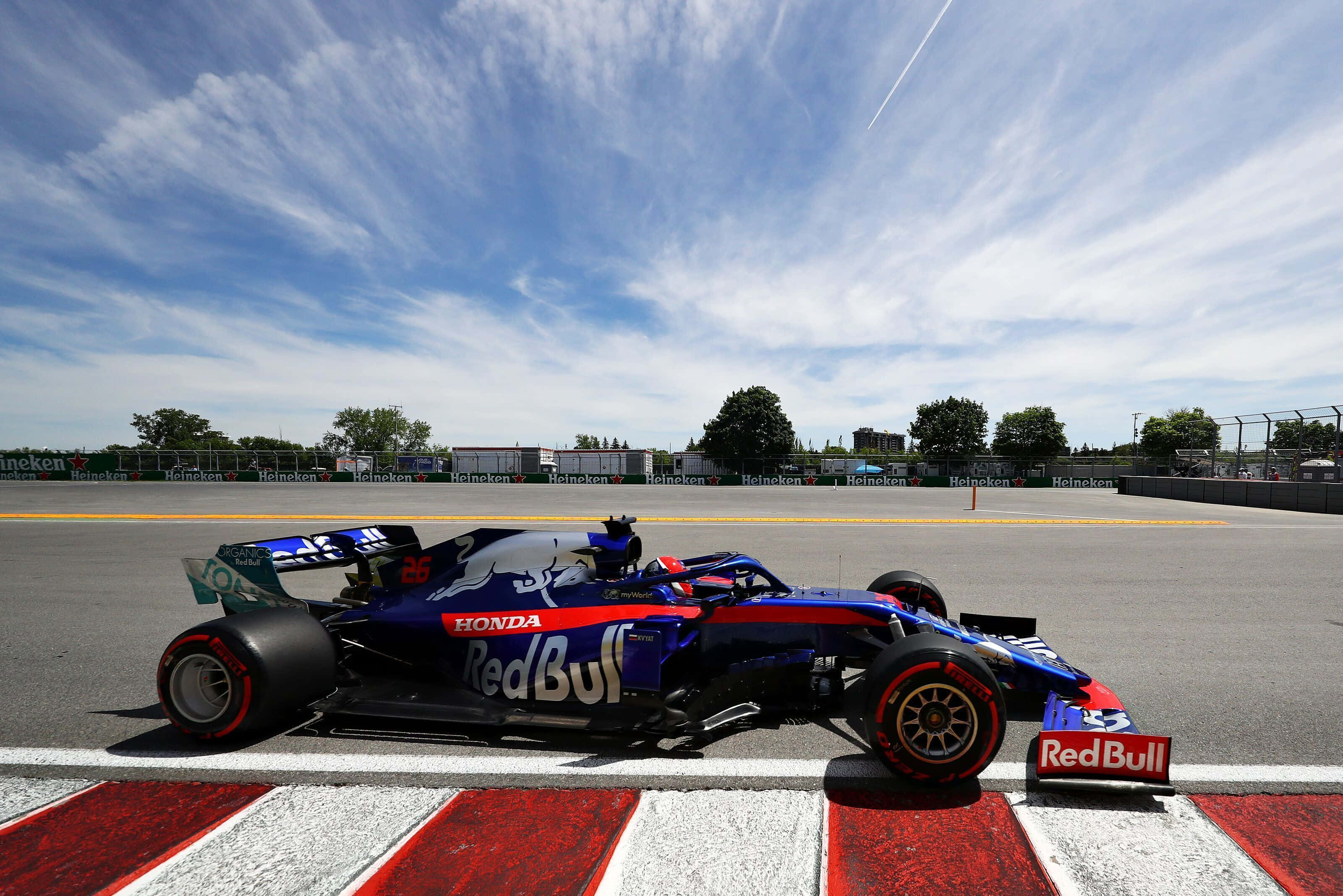 F1 2019 壁紙 桌布 壁紙 — 一輛紅牛車隊的一級方程式賽車，藍紅黑配色，停在賽道的紅色和白色路肩上，背景是晴朗的藍天和薄雲。