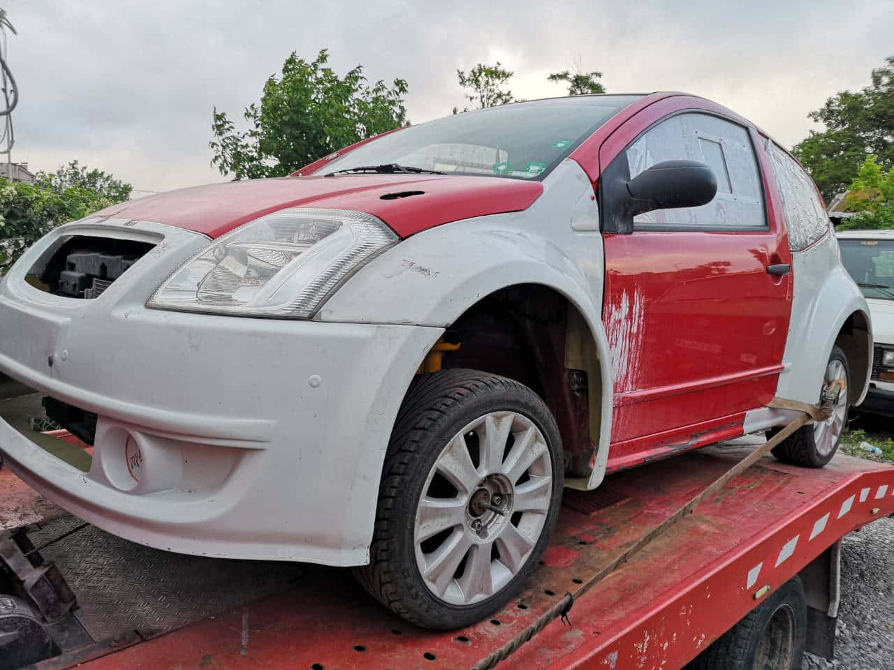 Citroen C2 Super 1600 桌布 壁紙 — 一輛紅白相間的小型車前部受損，停放在紅色平板拖車上，天空多雲。