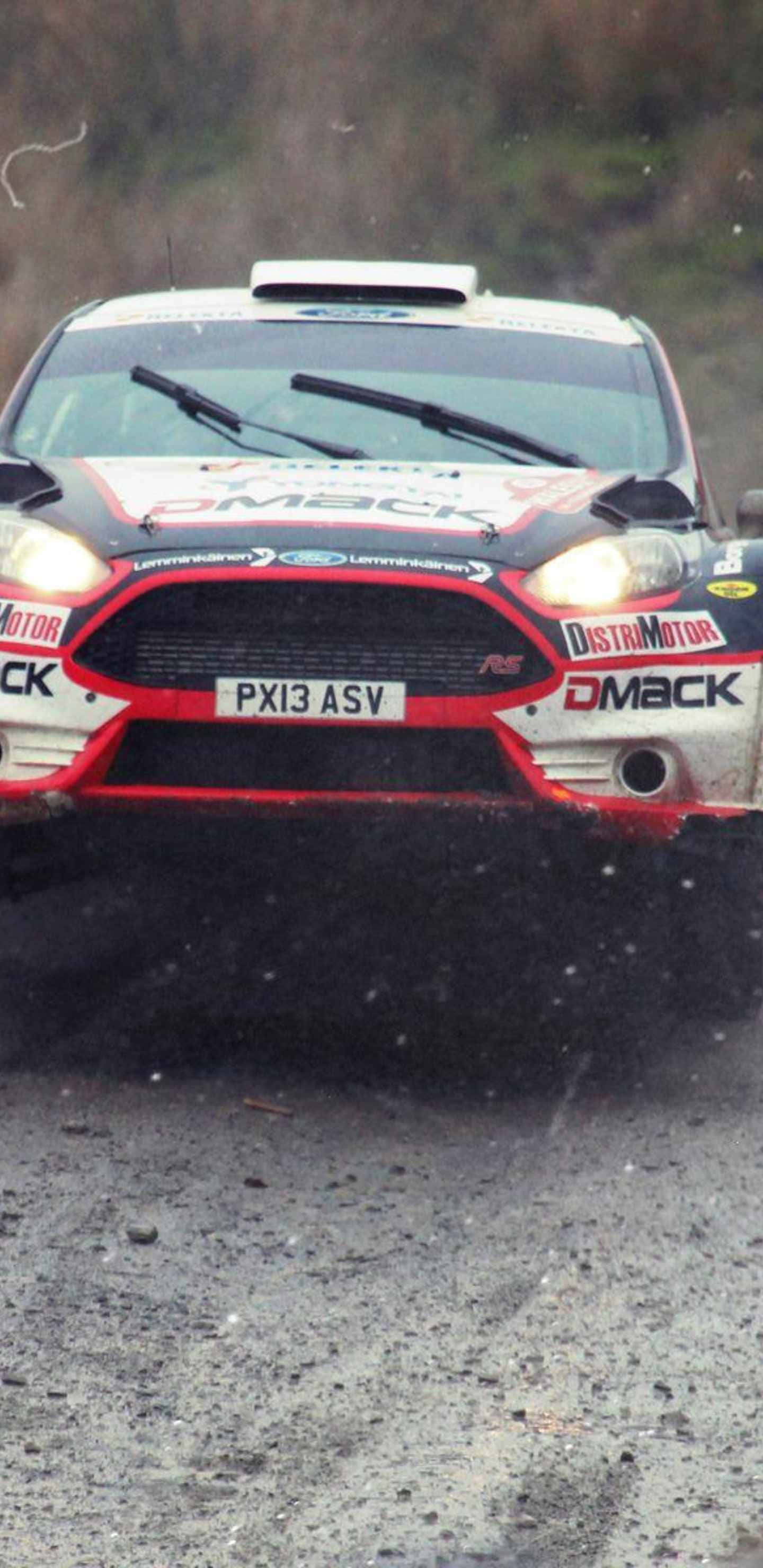 Android Dirt Rally 桌布 壁紙 — 一輛紅白相間的拉力賽車在森林地區的潮濕碎石路上飛馳，濺起泥漿。