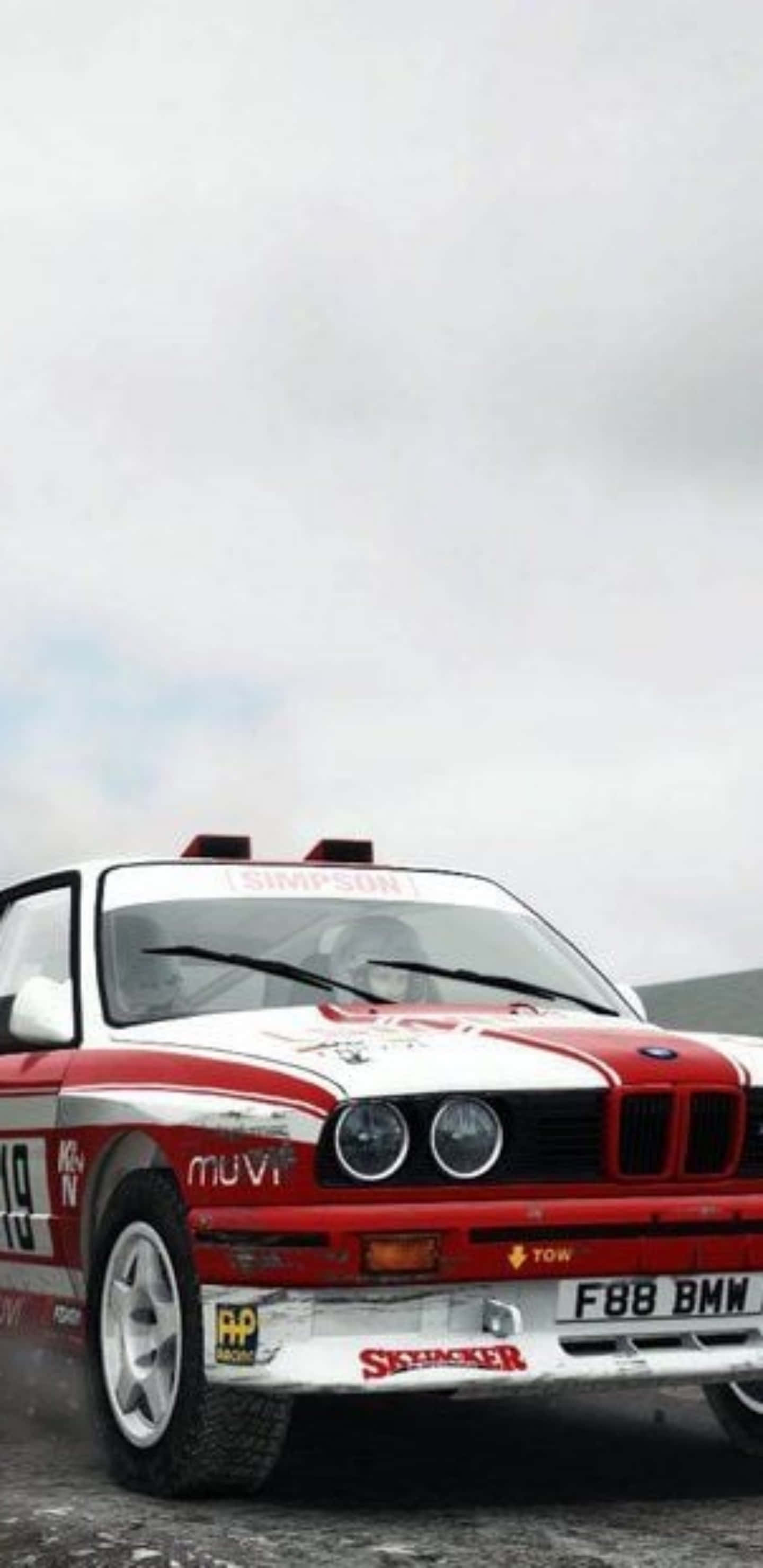 Pixel 3xl Dirt Rally 桌布 壁紙 — 一輛紅白相間的拉力賽車帶有贊助商貼紙，在多雲的天空下於濕滑道路上疾馳。