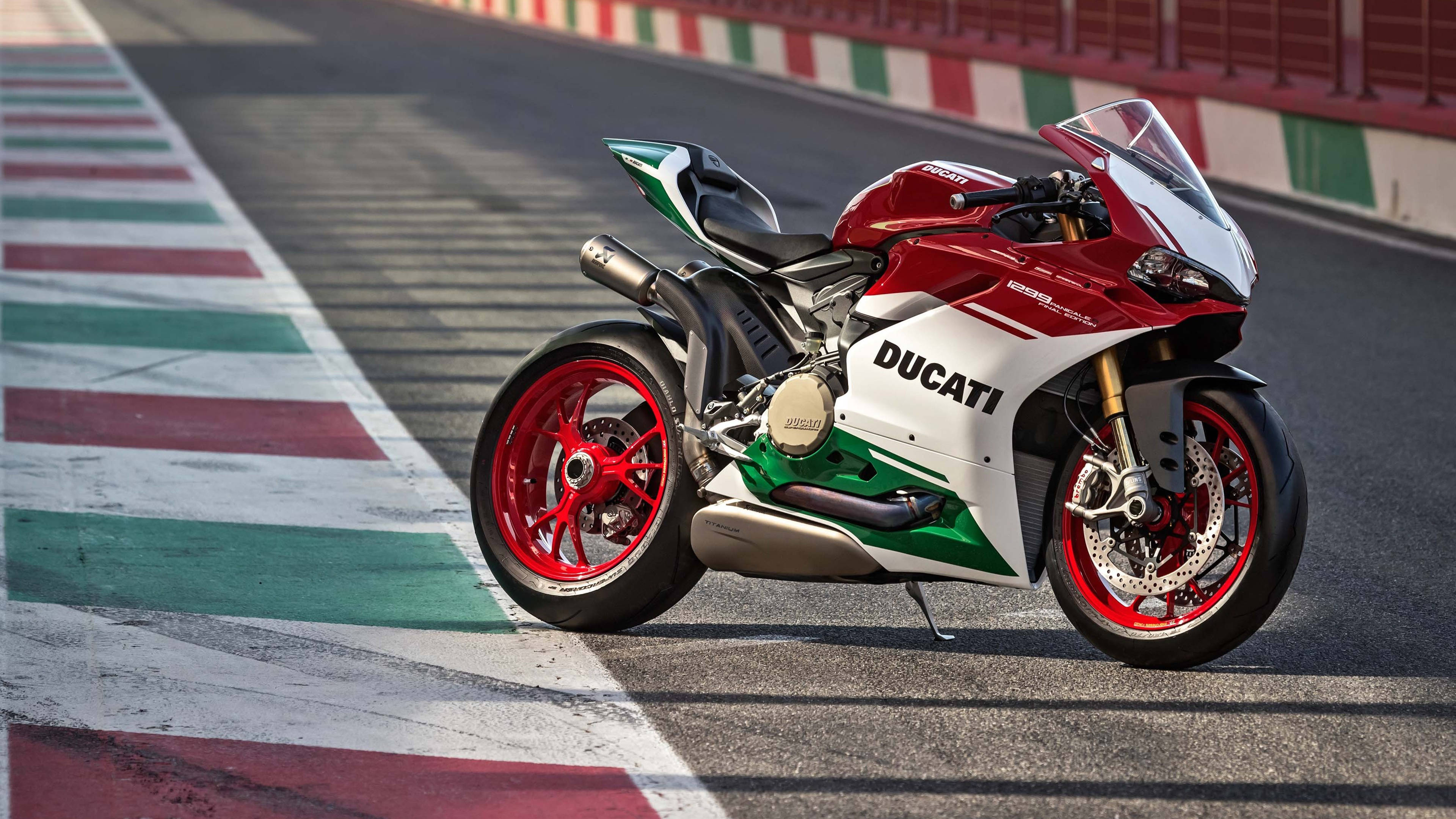 1920X1080 桌布 壁紙 — 一輛紅白綠色的Ducati摩托車停放在帶有義大利國旗顏色路緣的賽車場上。