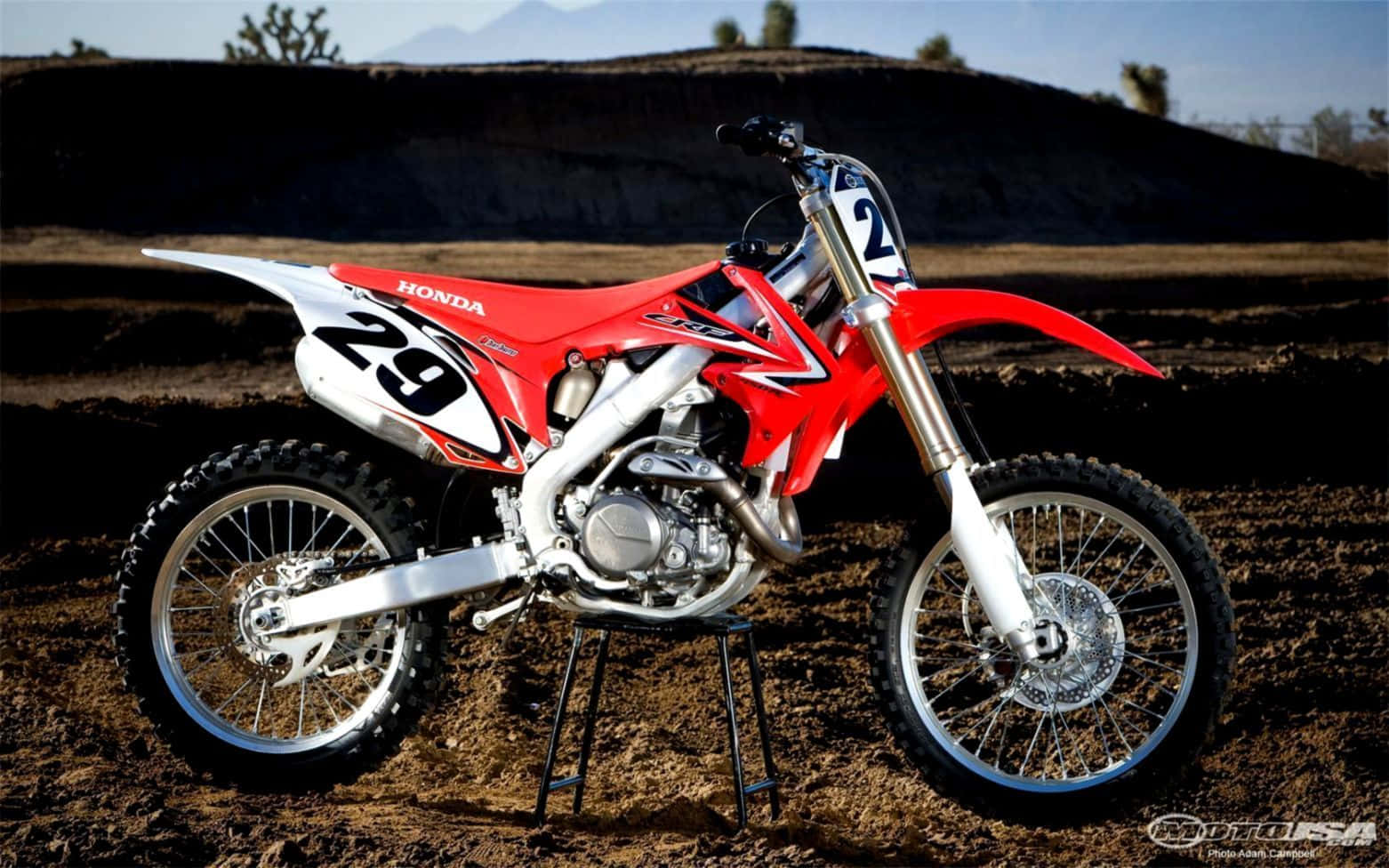 Ktm Bike 桌布 壁紙 — 一輛紅白色本田越野摩托車，號碼29，在明亮的日光下停放在泥土賽道上。