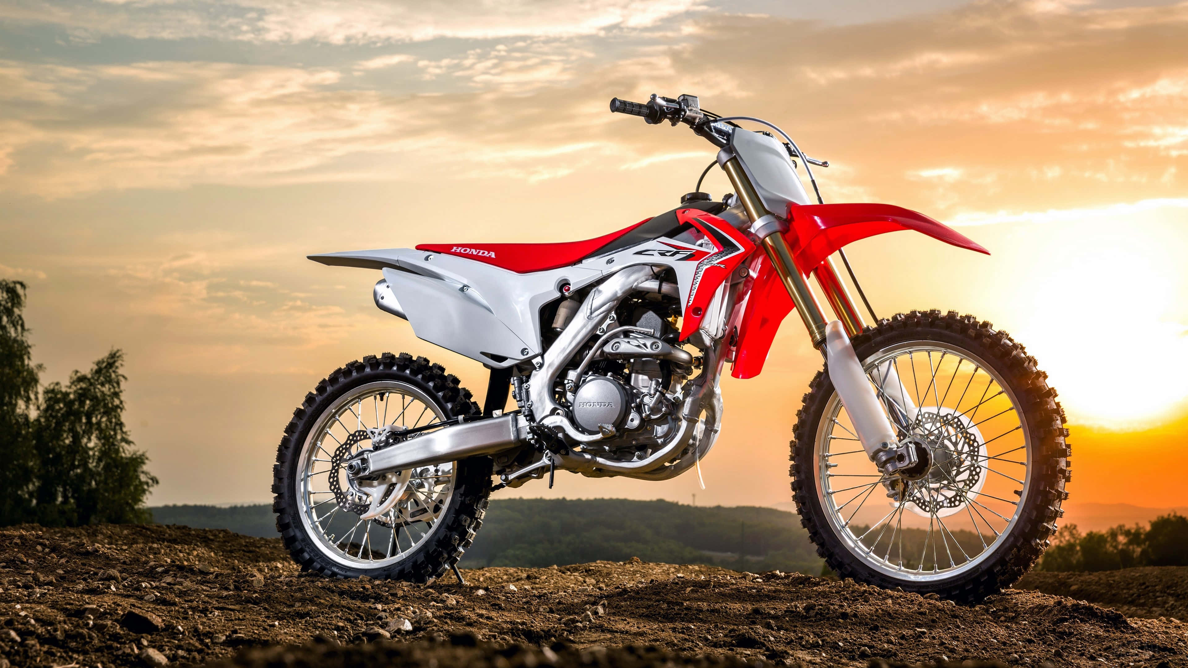 Motocross 桌布 壁紙 — 一輛紅白色本田越野機車在崎嶇地形上，襯著金黃色的日落天空。