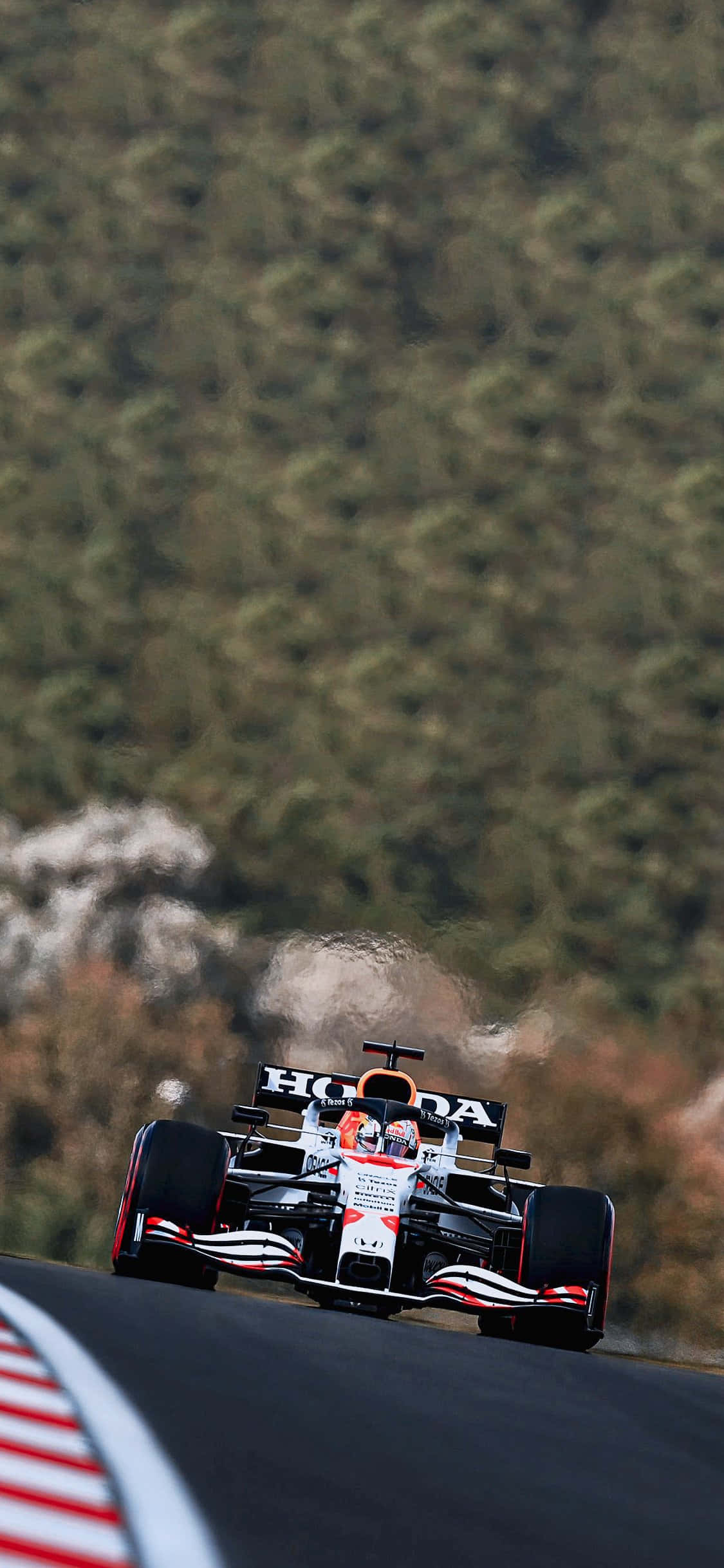 F1 桌布 壁紙 — 一輛紅白黑色的本田一級方程式賽車沿著蜿蜒的賽道疾馳，賽道兩旁是茂密的綠色森林。