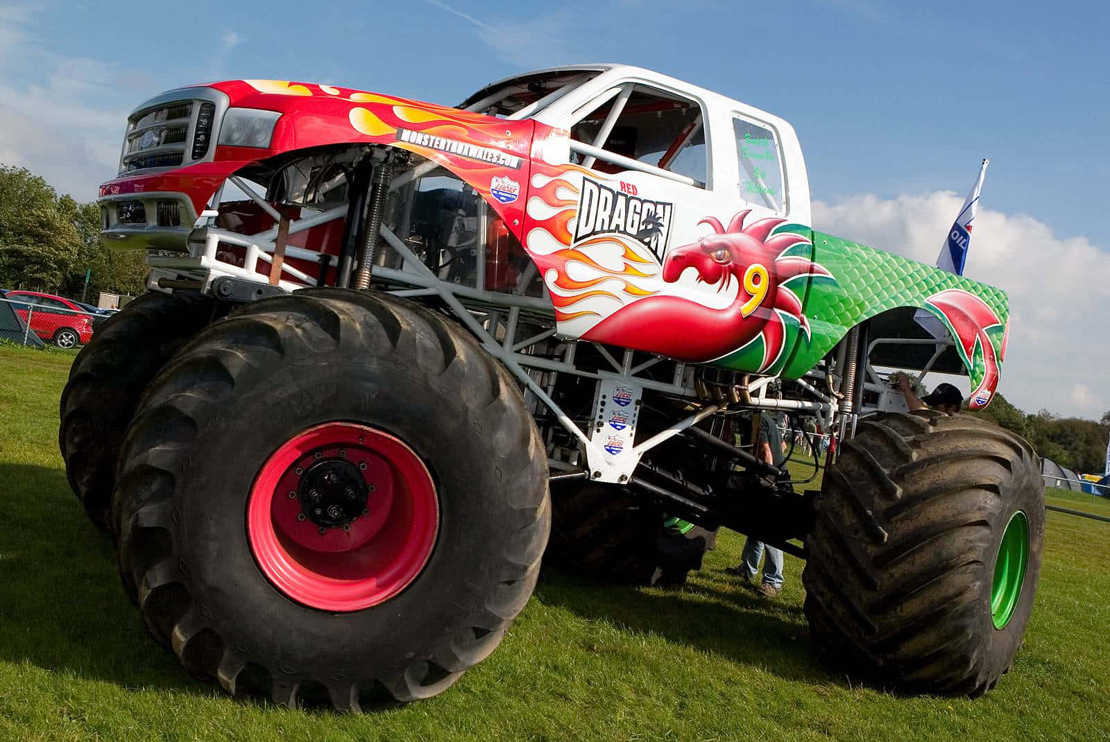 Monster Truck 桌布 壁紙 — 一輛紅綠相間、以龍為主題的怪獸卡車，配備巨大輪胎，停在藍天下的草地上。