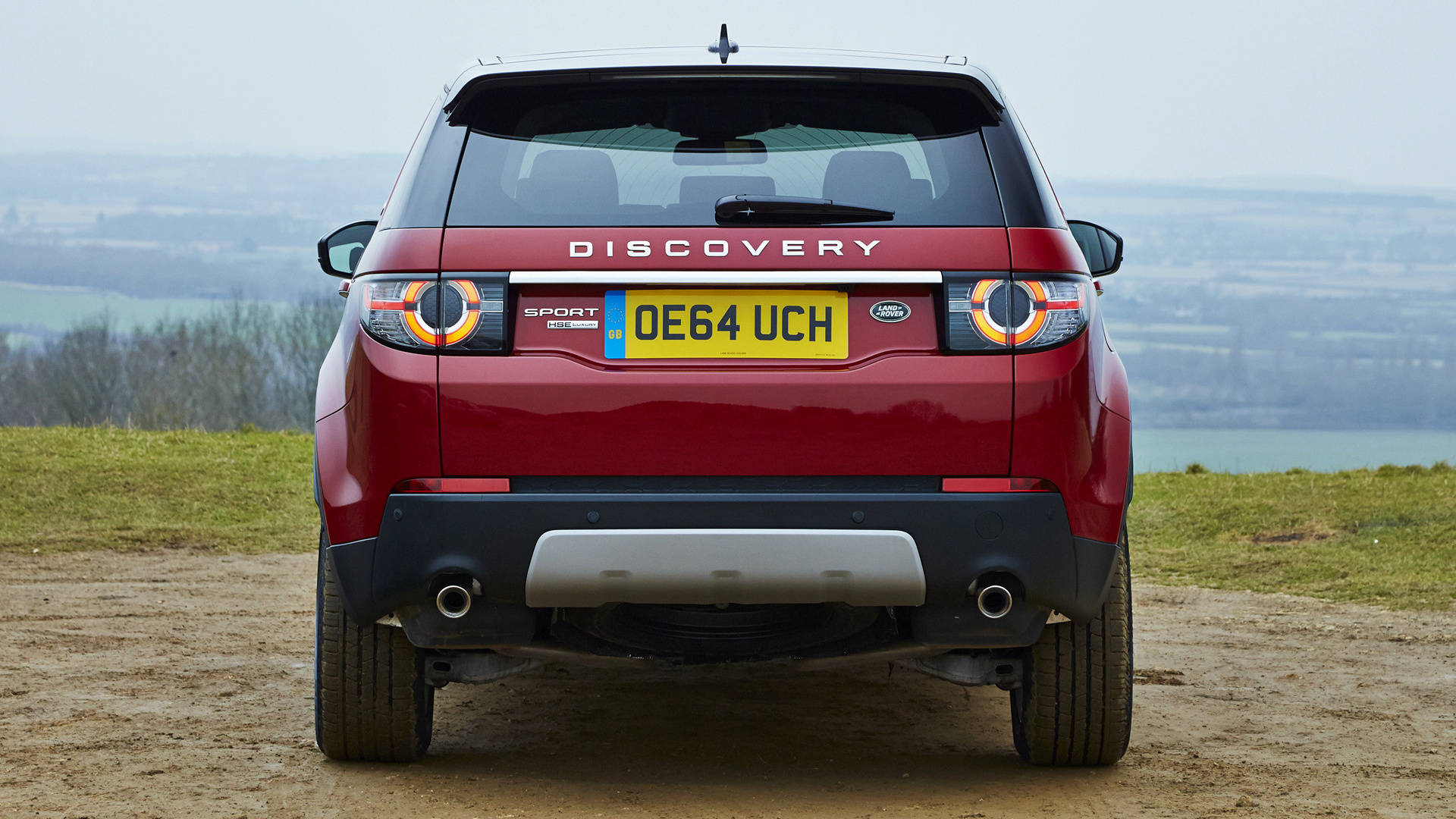 land rover iPhone 桌布 壁紙 — 一輛紅色 Land Rover Discovery Sport 停在一條泥路上，俯瞰著霧氣瀰漫的山谷，遠方有山丘和水面。